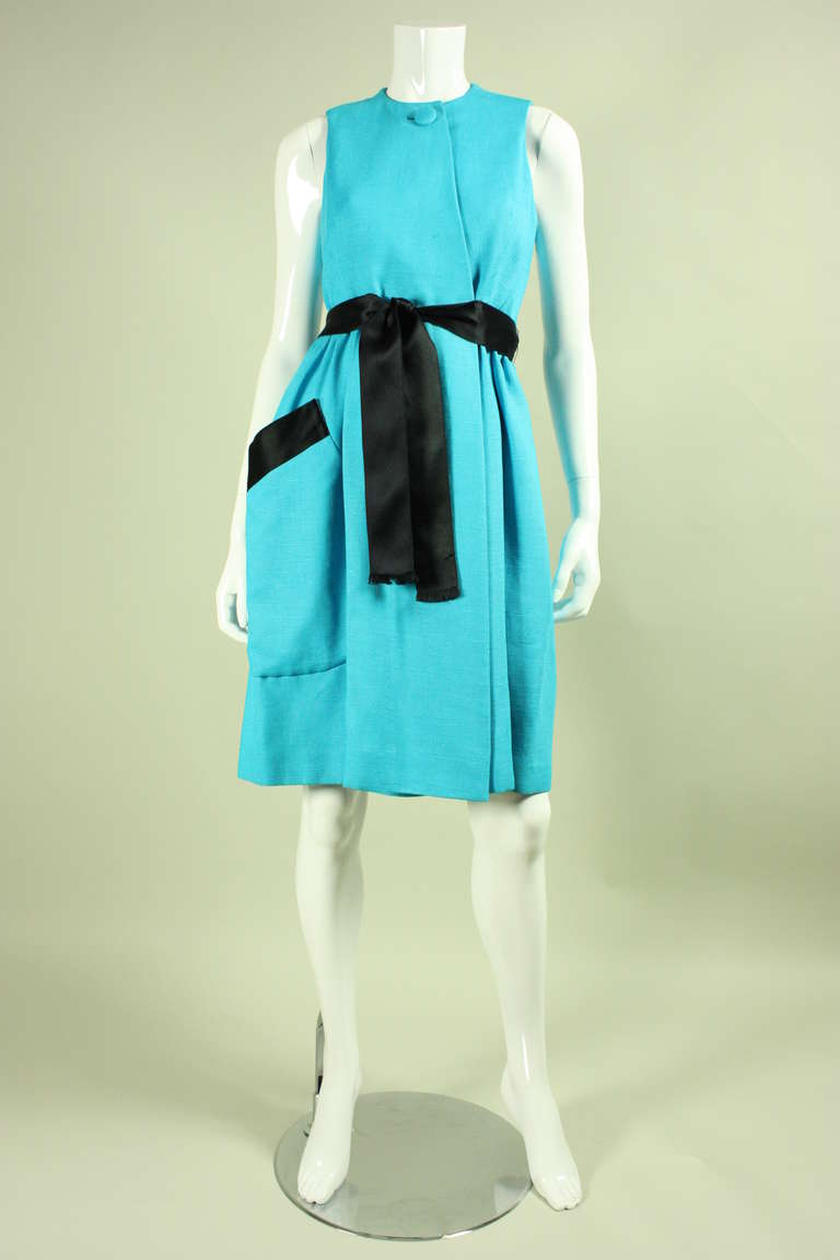 Vintage dress from American designer Geoffrey Beene dates to the 1960's.  It is made of turquoise linen with navy ribbon accents.  Dress is wrap-style with a covered button closure at front neck.  Large patch pocket.  Ribbon waist tie.  

No size