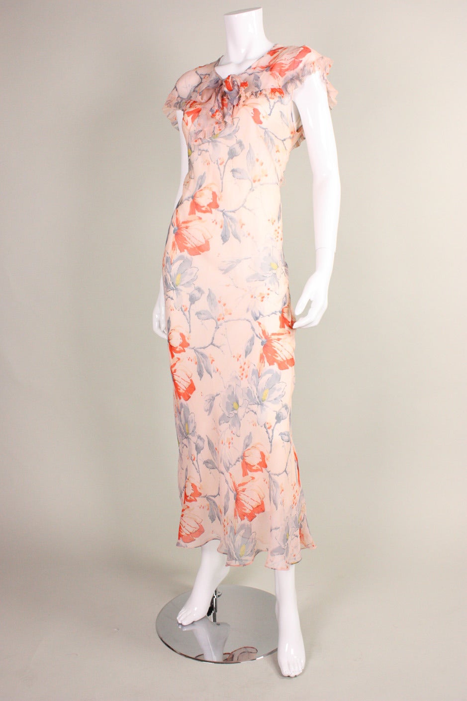 Lovely dress dates to the 1930's and is made of pale peach silk chiffon with a floral print in hues of orange and blue.  V-neck with center front bow and small key hole opening.  Middy collar with ruffled trim.  No closures.  Unlined but comes with