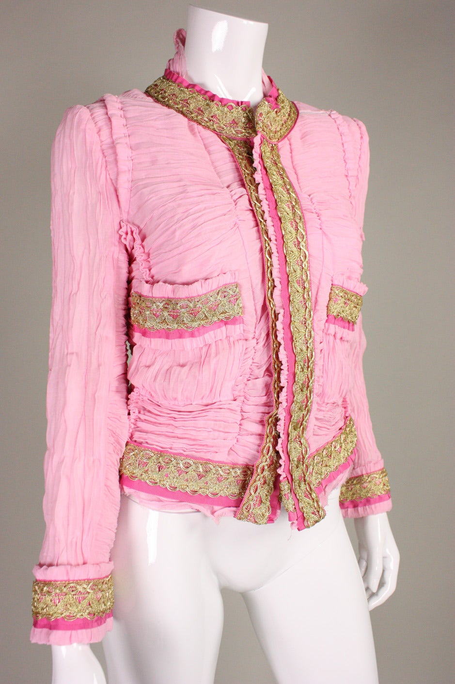 Comme des Garcons jacket by Junya Watanabe dates to 2007 and is made of pink material that is manipulated through ruching and pleating.  Metallic gold lace trim is backed by darker pink grosgrain ribbon.  Center front heavy-duty hook and eye