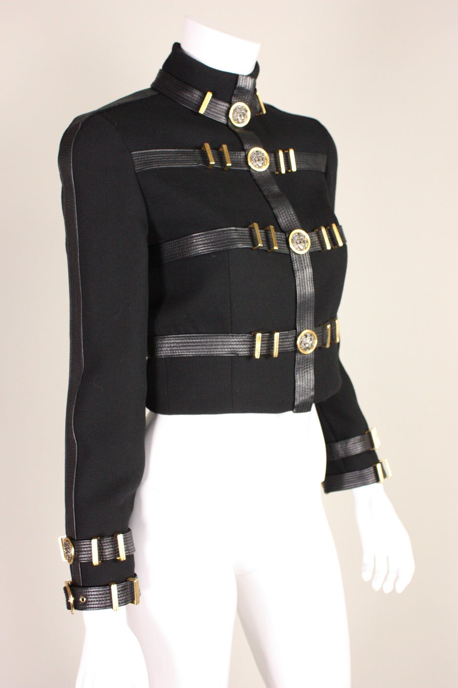Amazing and iconic vintage Versace cropped jacket dates to 1992 and is made of black wool with leather trim.  Metal hardware with Medusa medallions down center front and at cuffs.  Center front covered snap closures.  Fully lined.

No size label,