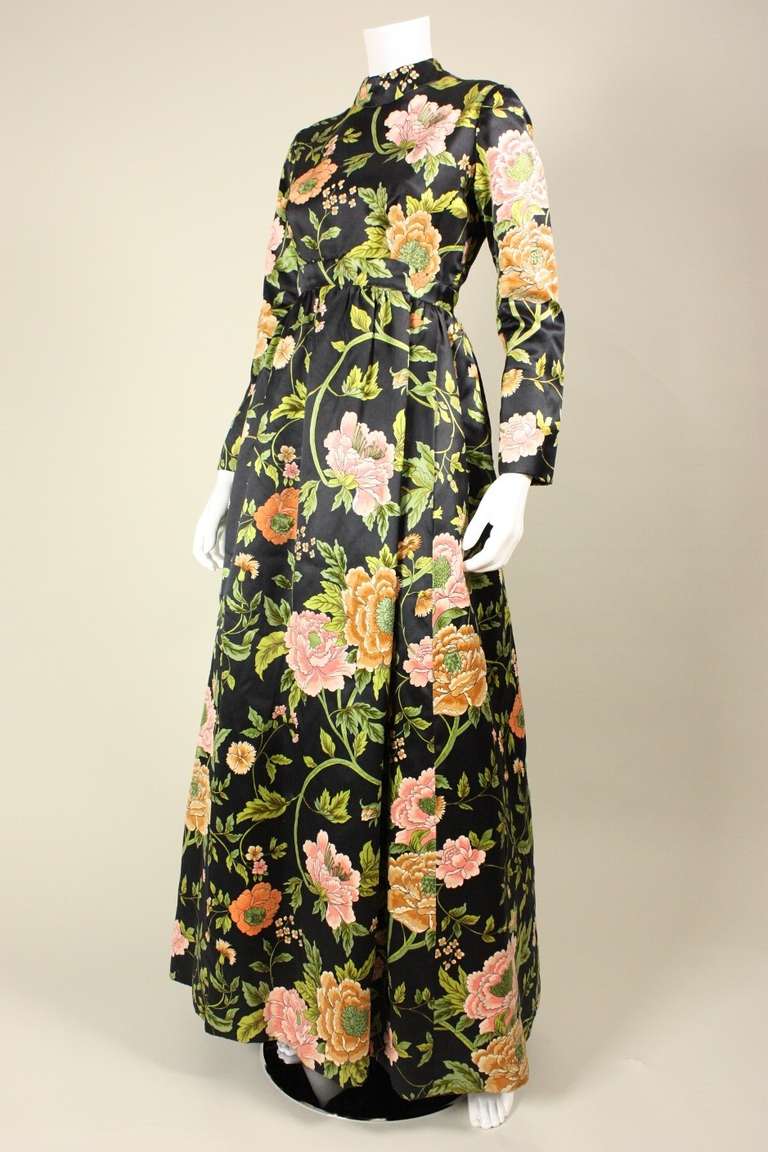 Timeless gown from George Halley dates to the 1960's and is made of black silk satin with multicolored flowers and leaves that have a raised velvet pile.  Fitted bodice has mock neck and long sleeves.  Floor-length skirt is gathered all along