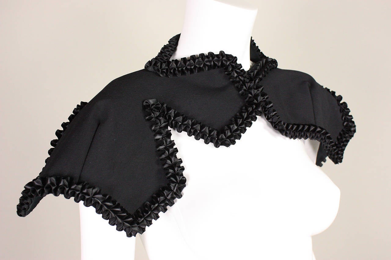 Comme des Garcons black shrug has shirred satin ribbon trim and asymmetrical collar.  Center front hook and eye closure.  Unlined.  Circa 2008

Labeled size Small.  New with tags.