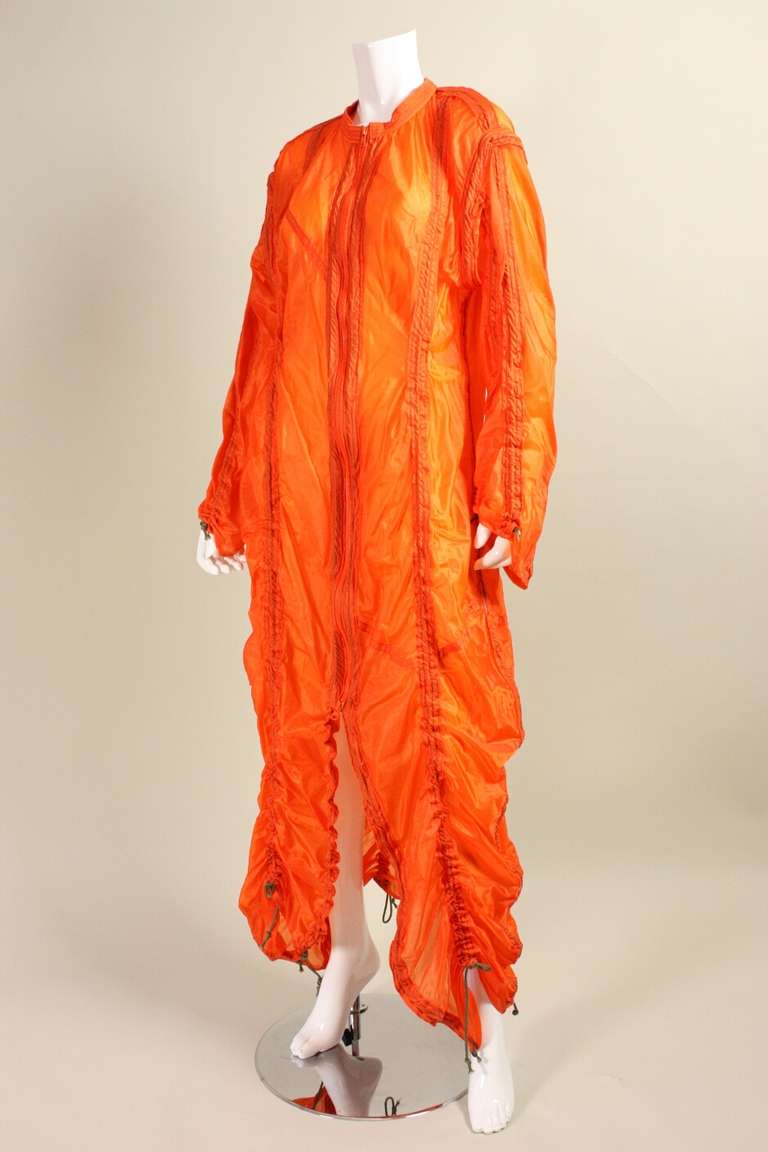Iconic parachute jacket from Norma Kamali's OMO line dates to the late 1970's to the early 1980's. It is made of orange ripstop with vertical drawstrings that can be cinched to form narrow gathers. Round neck. Center front zip closure.