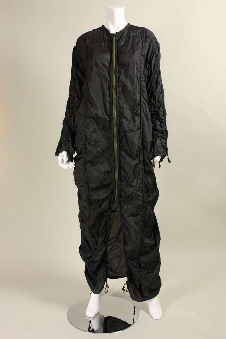 Iconic parachute jacket from Norma Kamali's OMO line dates to the late 1970's to the early 1980's.  It is made of black nylon with vertical drawstrings that can be cinched to form narrow gathers.  Round neck.  Center front zip closure. 