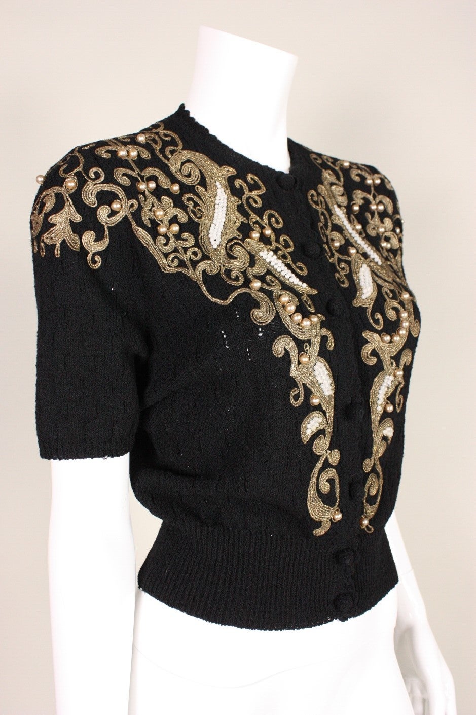 Vintage sweater likely dates to the 1950's and is made of a black knit.  Gold bullion trim with beaded accents adorns the center front, partially down the sleeves, and across the back shoulders.  Center front button closure.  Unlined.  There is no