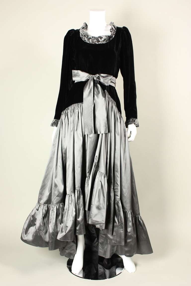 Vintage Yves Saint Laurent gown dates to the early 1980's.  Black velvet bodice has a scoop neck and long sleeves, both of which have a taffeta ruffle trim.  Drop-waisted asymmetrical skirt is made of gunmetal gray silk taffeta and has a wide ruffle