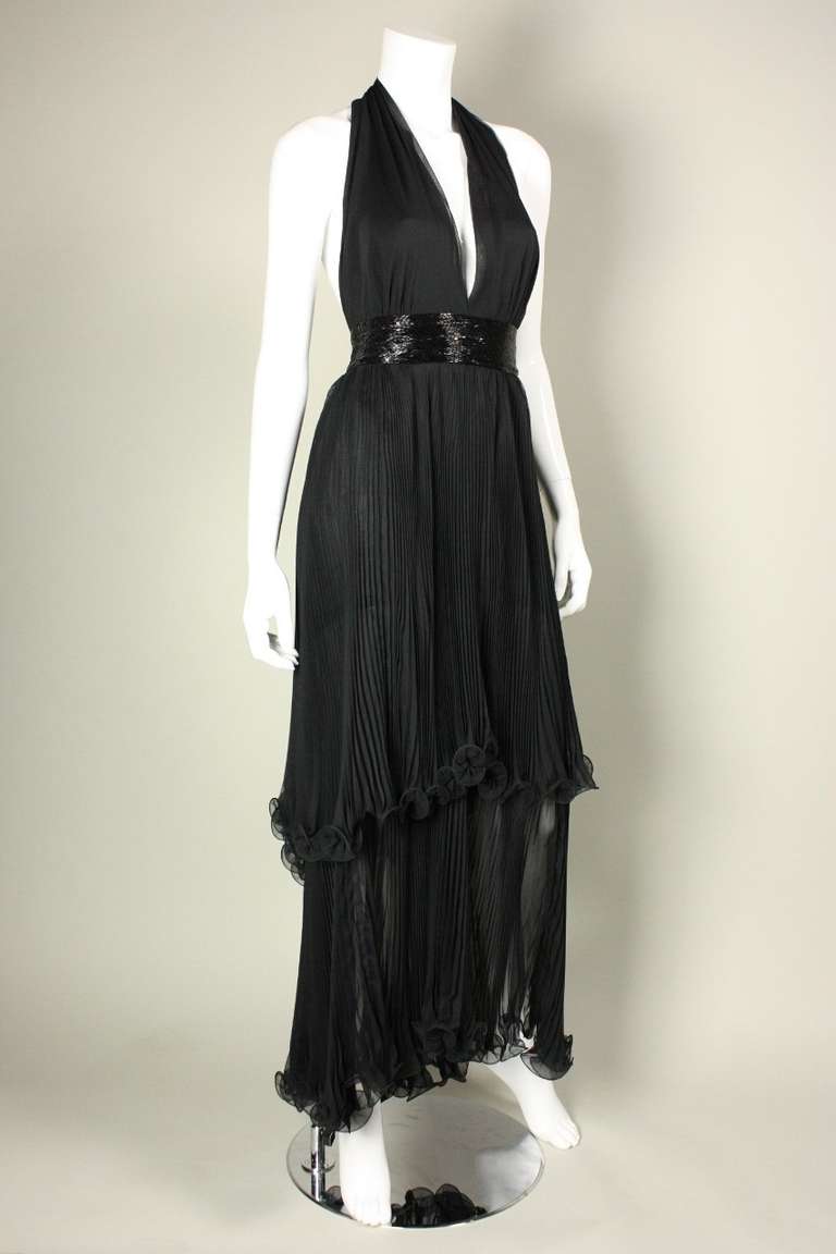 Fabulous gown and capelet from Alfred Bosand is made of black pleated chiffon and dates to the 1970's.  Dress has plunging v-neck, open back, beaded waistband, and tiered skirt.  Matching capelet has center front hook and eye closure and beaded