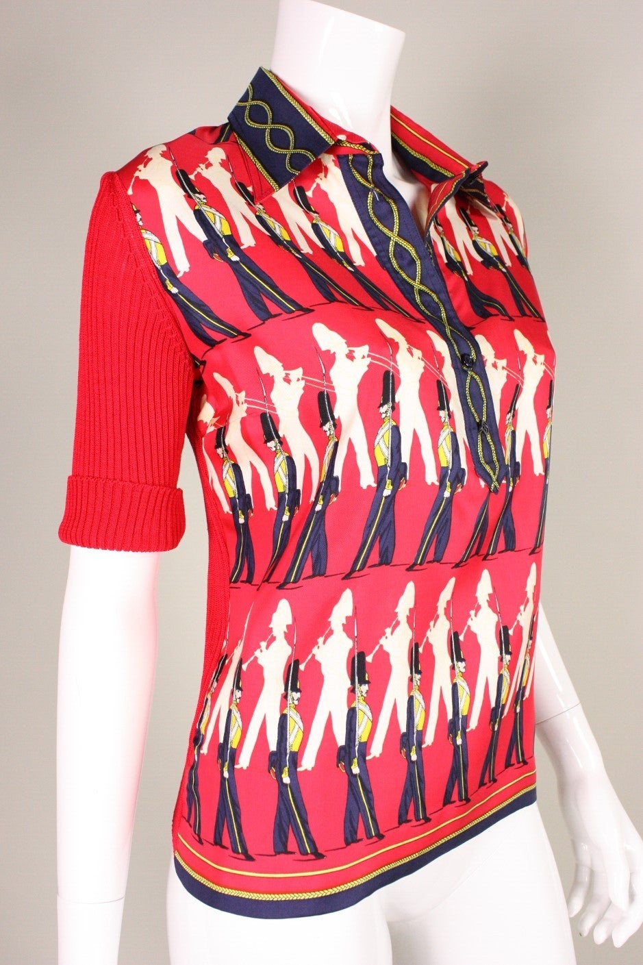 Vintage Hermès sweater dates to the 1960's and has a silk front and ribbed cotton knit back in tones of red.  Front features a soldier print in cream, navy and yellow.  Center front placket has button closure,  Turn down collar. Unlined.

Labeled