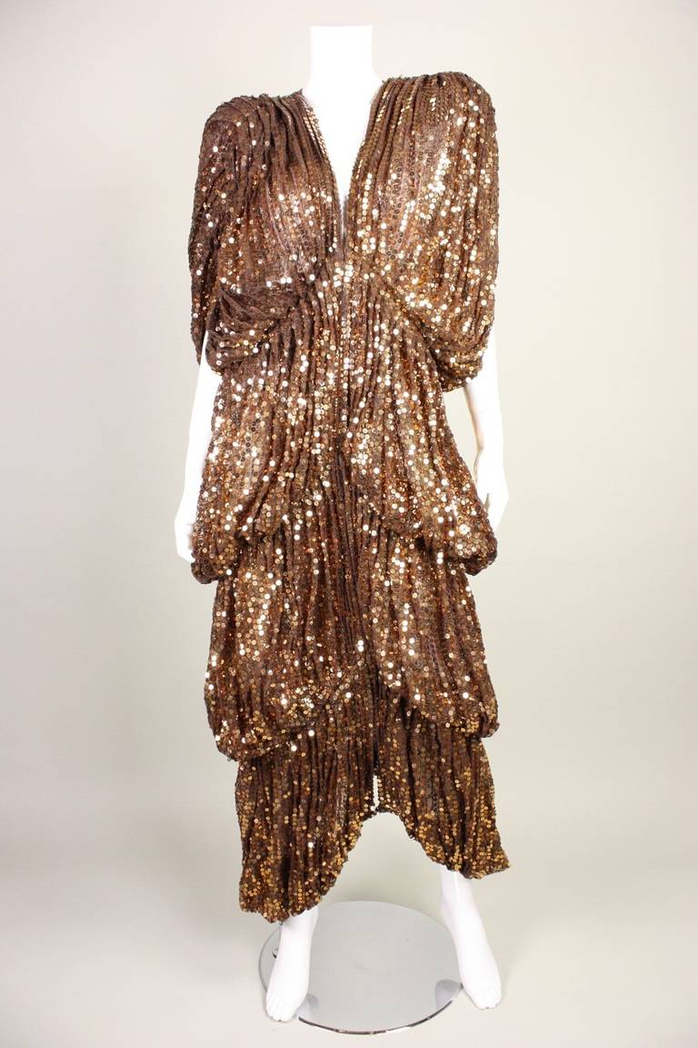 Vintage Norma Kamali OMO dress or coat dates to the late 1970's through early 1980's.  It is made of sheer brown fabric that is covered in rows of bronze sequins.  Deep v-neck.  Heavily padded shoulders.  Center front heavy duty hook and eye