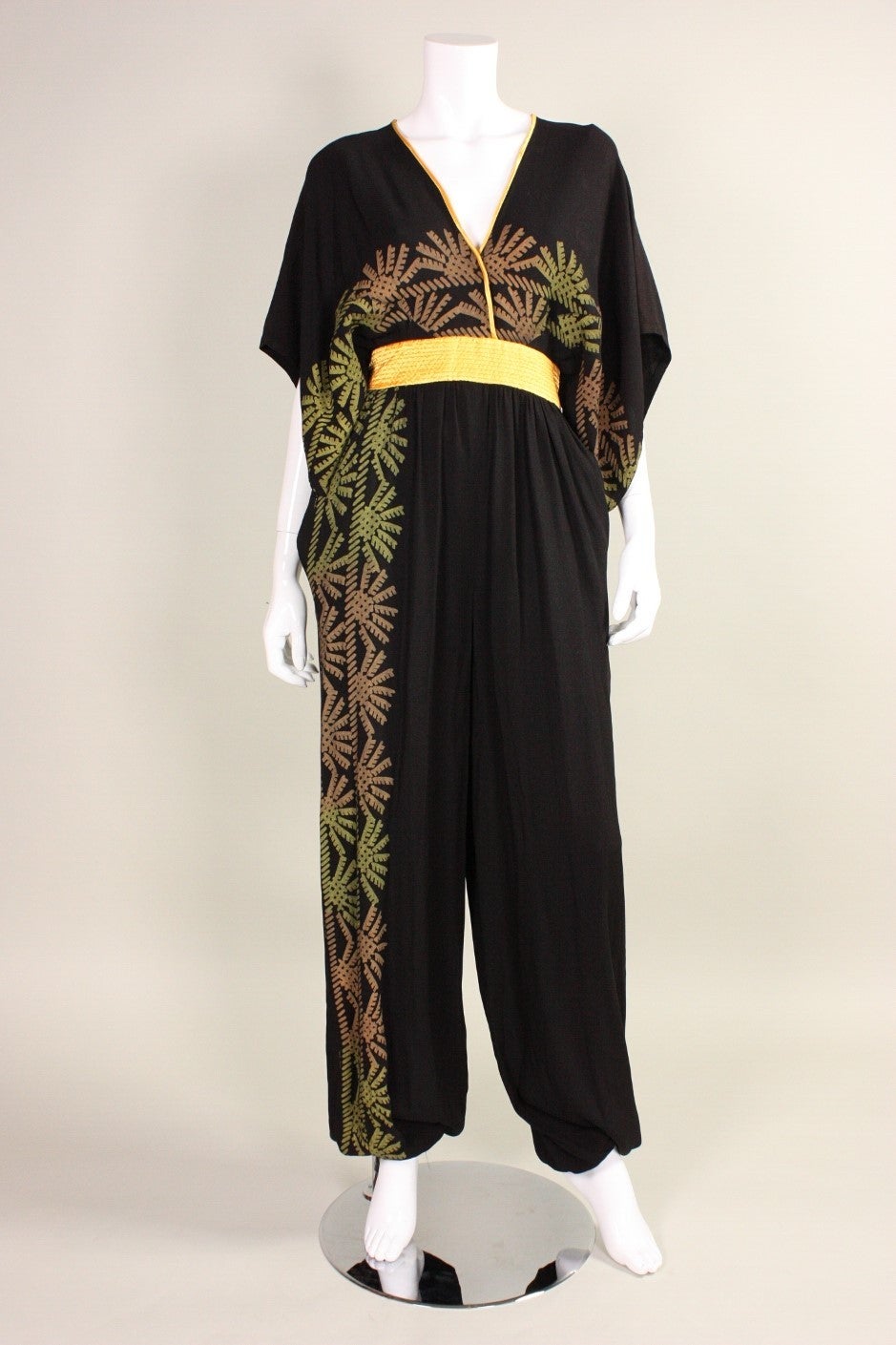 Vintage jumpsuit from Zandra Rhodes dates to the 1980's and retailed at Neiman Marcus.  It is made of black crepe with a geometric hand screen-print in shades of rust orange and yellow.  Marigold satin waistband and piping around neckline. Pant