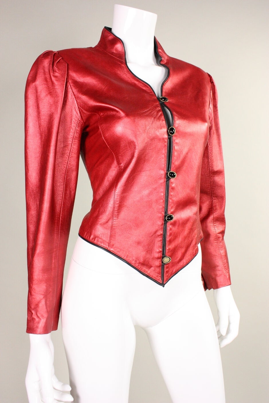 Vintage jacket from Emanuel Ungaro dates to the 1980's and is made of metallic red leather. It is fitted throughout, has a stand collar, and button front closure.  Long sleeves are gathered at the padded shoulder and have button cuffs. Trimmed in