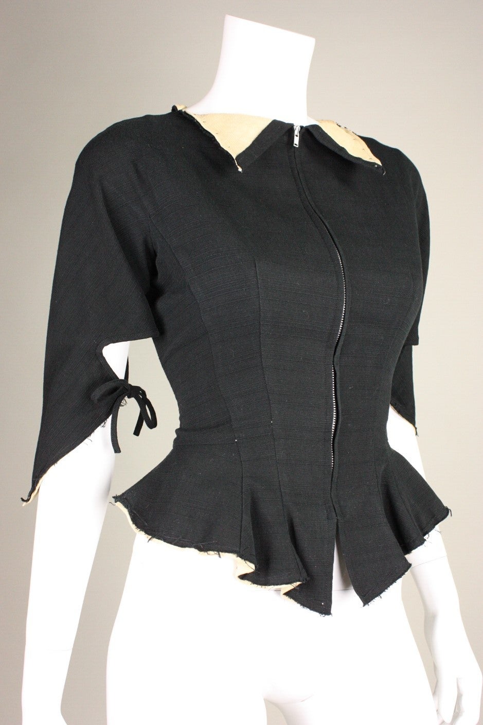 Fitted jacket from Yohji Yamamoto is made of black cotton with contrasting beige collar and cuffs.  3/4-length sleeves with open detail and ties at inner elbows.  Nipped waist with peplum.  Partially lined.  Center front zippered closure.

Labeled