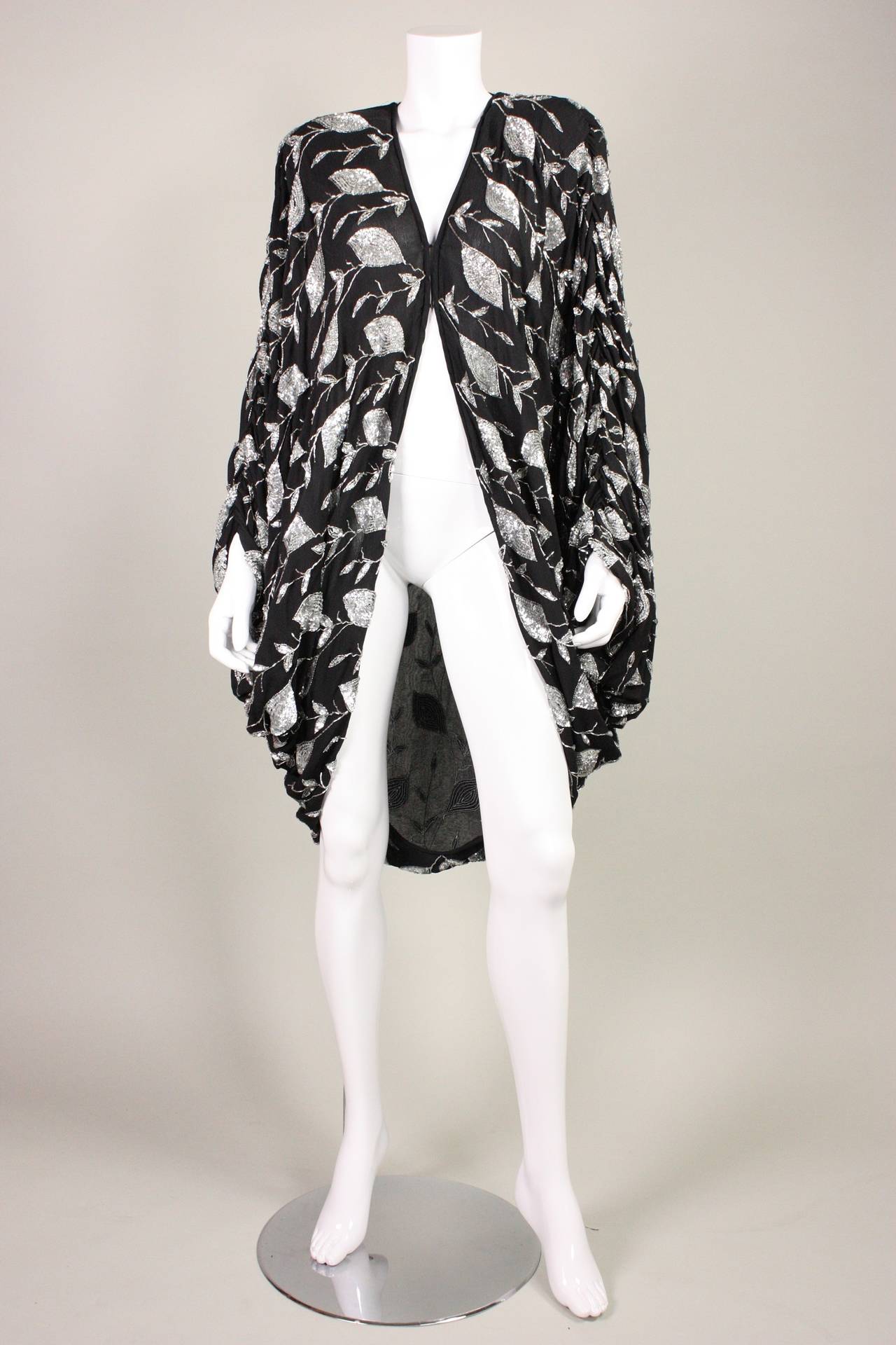Vintage cocoon coat dates to the 1980's and is made of black chiffon that is adorned with silver sequins and beading in a leaf-like pattern.  Unlined.  Center front double hook and eye closure at bust.  Large shoulder pads.

No size label. 