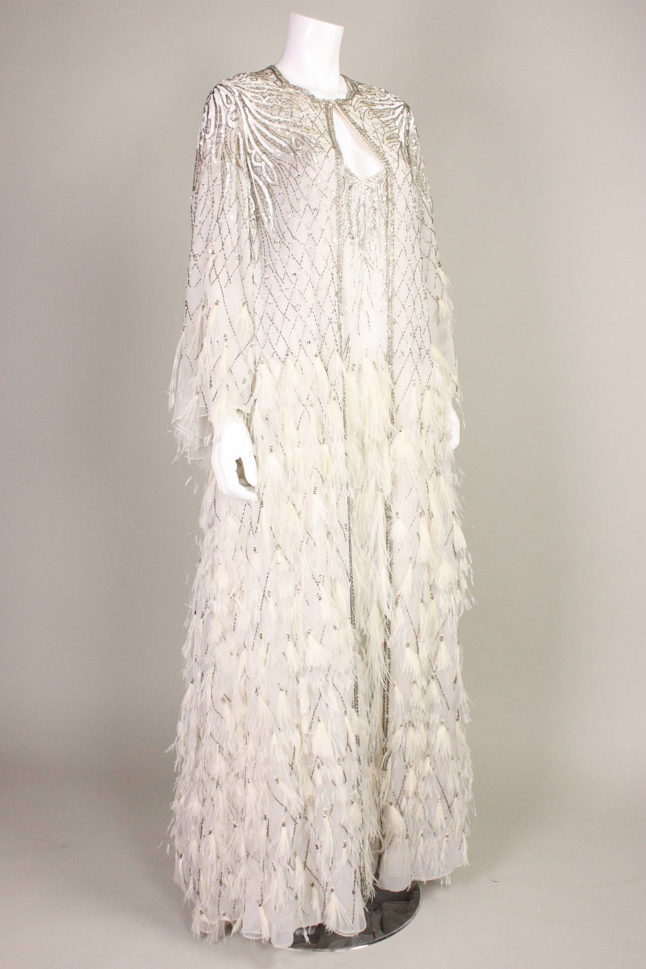 Fabulous gown and coat from Ruben Panis are made of white chiffon that is adorned with white feathers, rhinestones, sequins, and beading.  Long sleeved coat is floor-length and fastens at the center front neck with a hook and eye closure.  Sexy gown