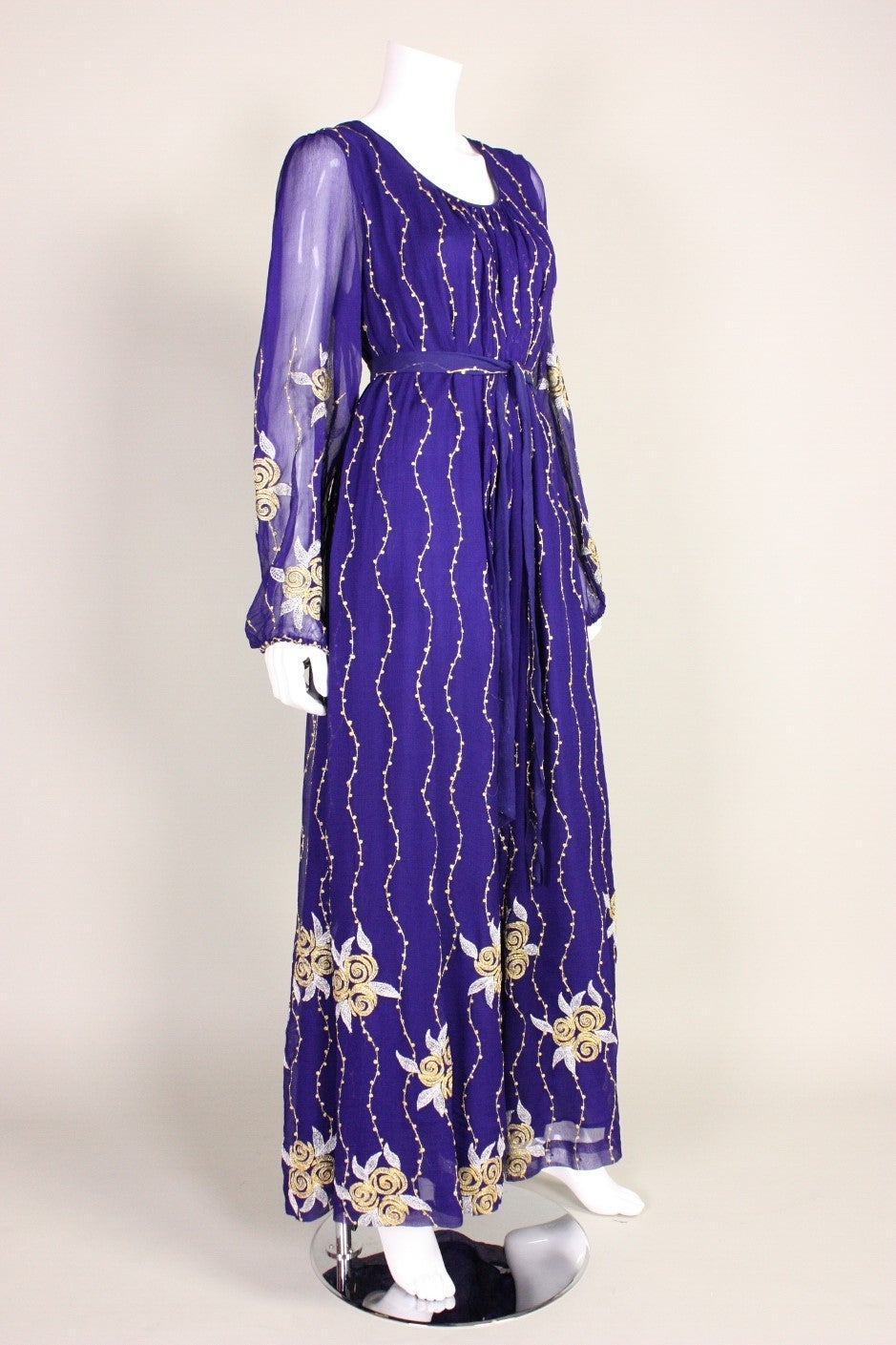 Vintage maxi dress from Raksha retailed at I. Magnin and dates to the 1970's.  It is made of purple silk chiffon with gold and white machine embroidery.  Scoop neckline.  Lined except for in sleeves.  Center back zipper closure.  Can be worn with or