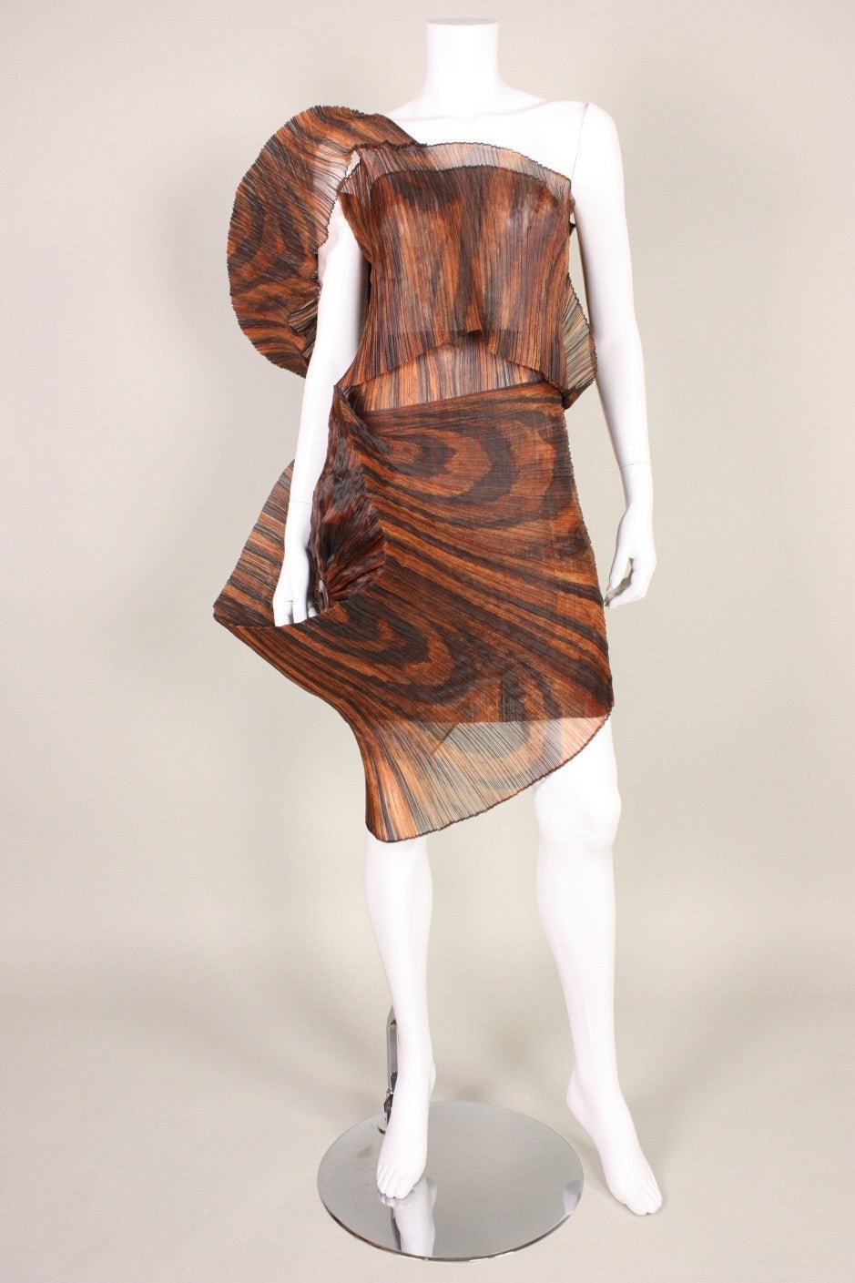 Vintage ensemble from Issey Miyake's Flower Pleats Series dates to his Spring/Summer 1990 collection.  It is made of 100% heat set polyester with a brown and black woodgrain print.  Large sculptural circular forms are created on blouse and skirt