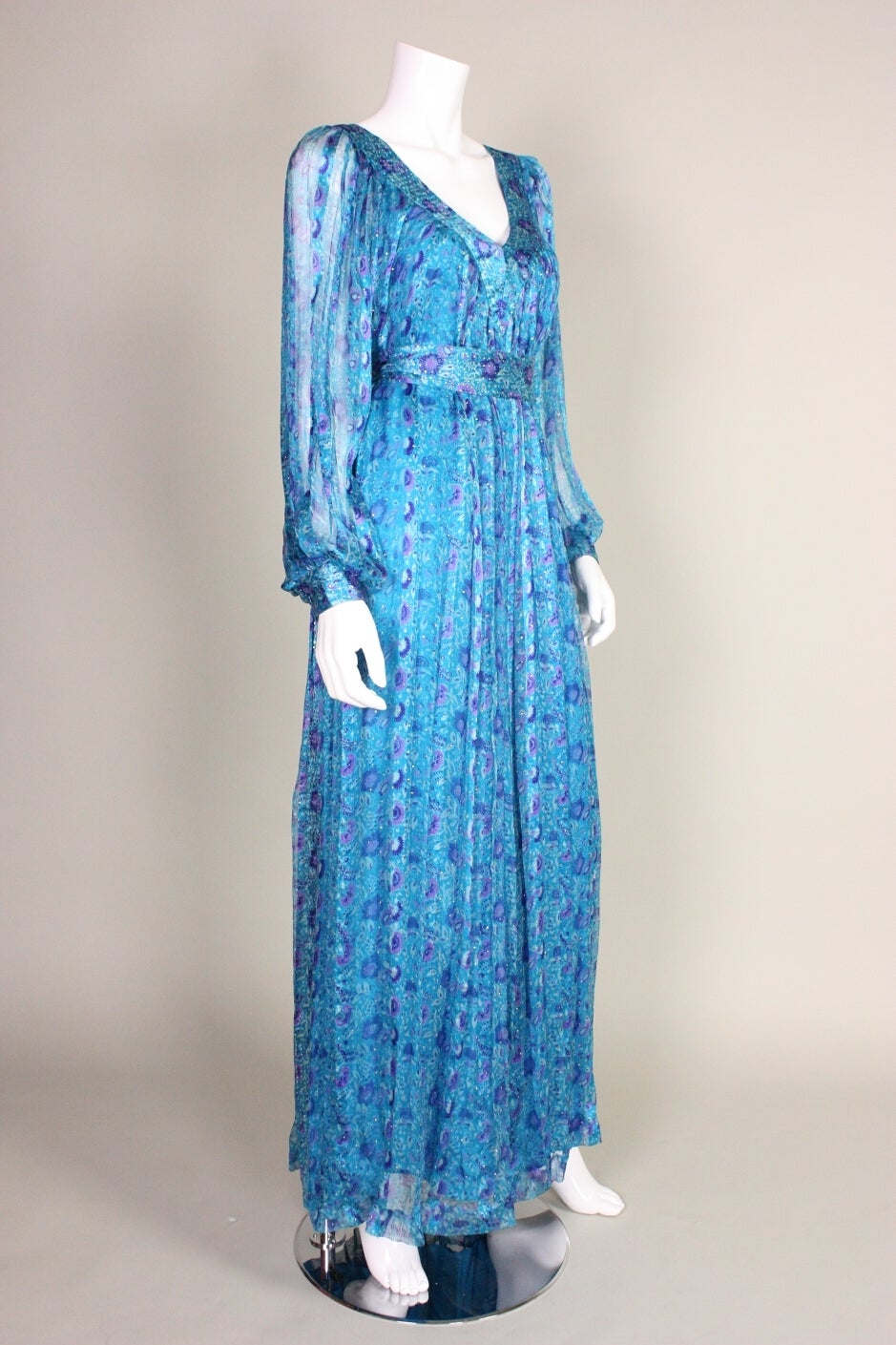 Vintage maxi dress from Raksha retailed at I. Magnin and dates to the 1970's. It is made of turquoise silk chiffon with a floral print and tiny pieces of metal clamped in (like an assuit). V neckline. Lined except for in sleeves. Center back zipper