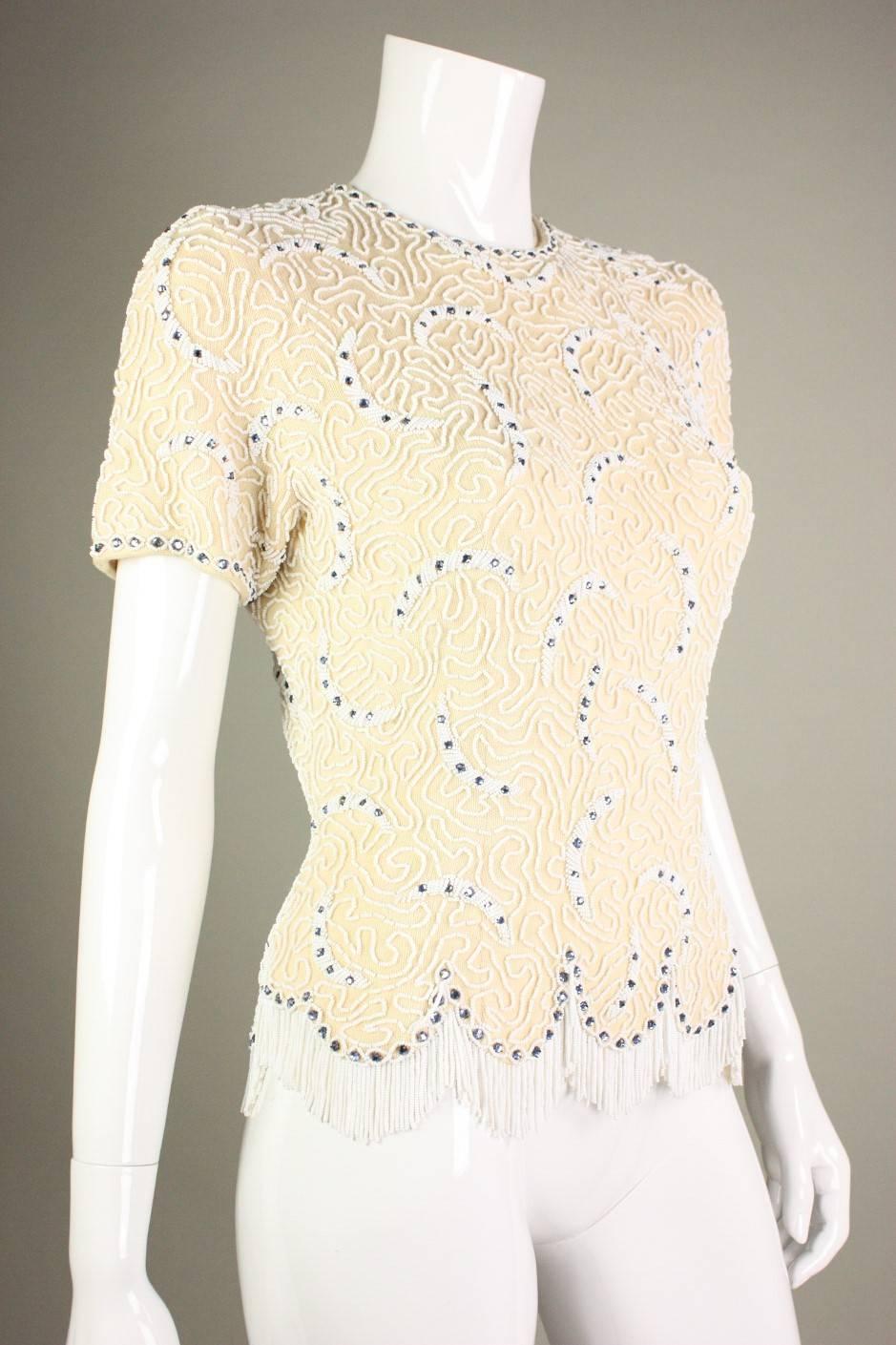 Vintage sweater from Elsie Tu dates to the 1950's through early 1960's and is made of cream-colored wool.  It is decorated with white seed beads in a squiggle pattern and highlighted with sapphire blue, prong-set rhinestones.  Scalloped hem has