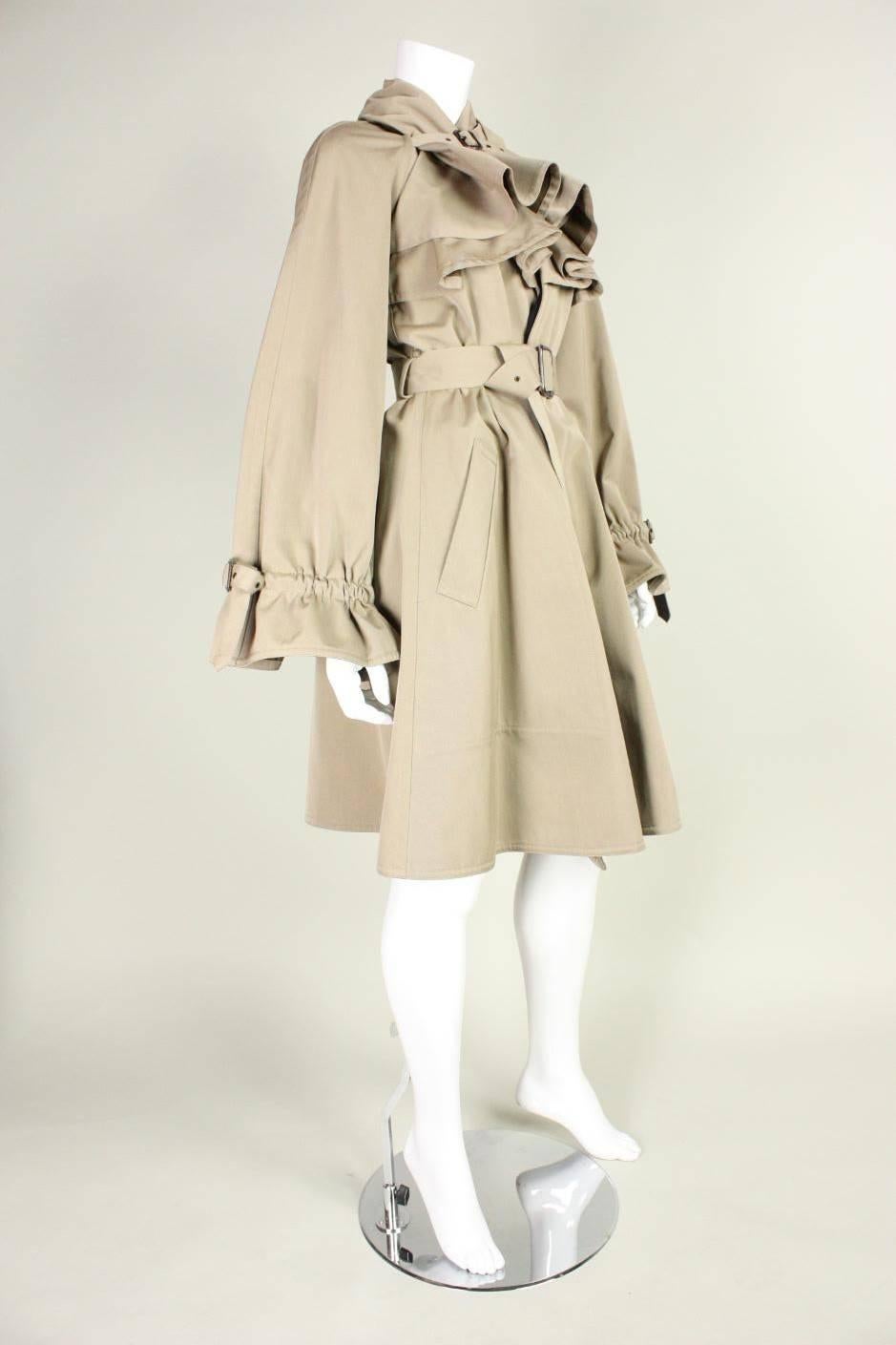 Trench rain coat from Jean-Paul Gaultier is made of tan fabric with a waterproof backing.  Neckline can be worn two ways (as shown).  Wide sleeves are gathered at wrists.  Hip pockets.  Detached belt.  Unlined except for throughout bust, where it is
