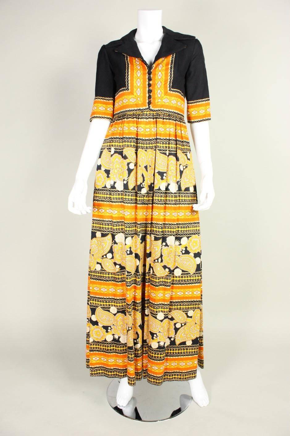 Jumpsuit from Oscar de la Renta Boutique dates to the 1970's.  Black cotton pique bodice has v-neck, turn down collar, and decorative covered buttons down the center front.  Wide pant legs are made of brightly fabrics in hues of yellow and orange. 