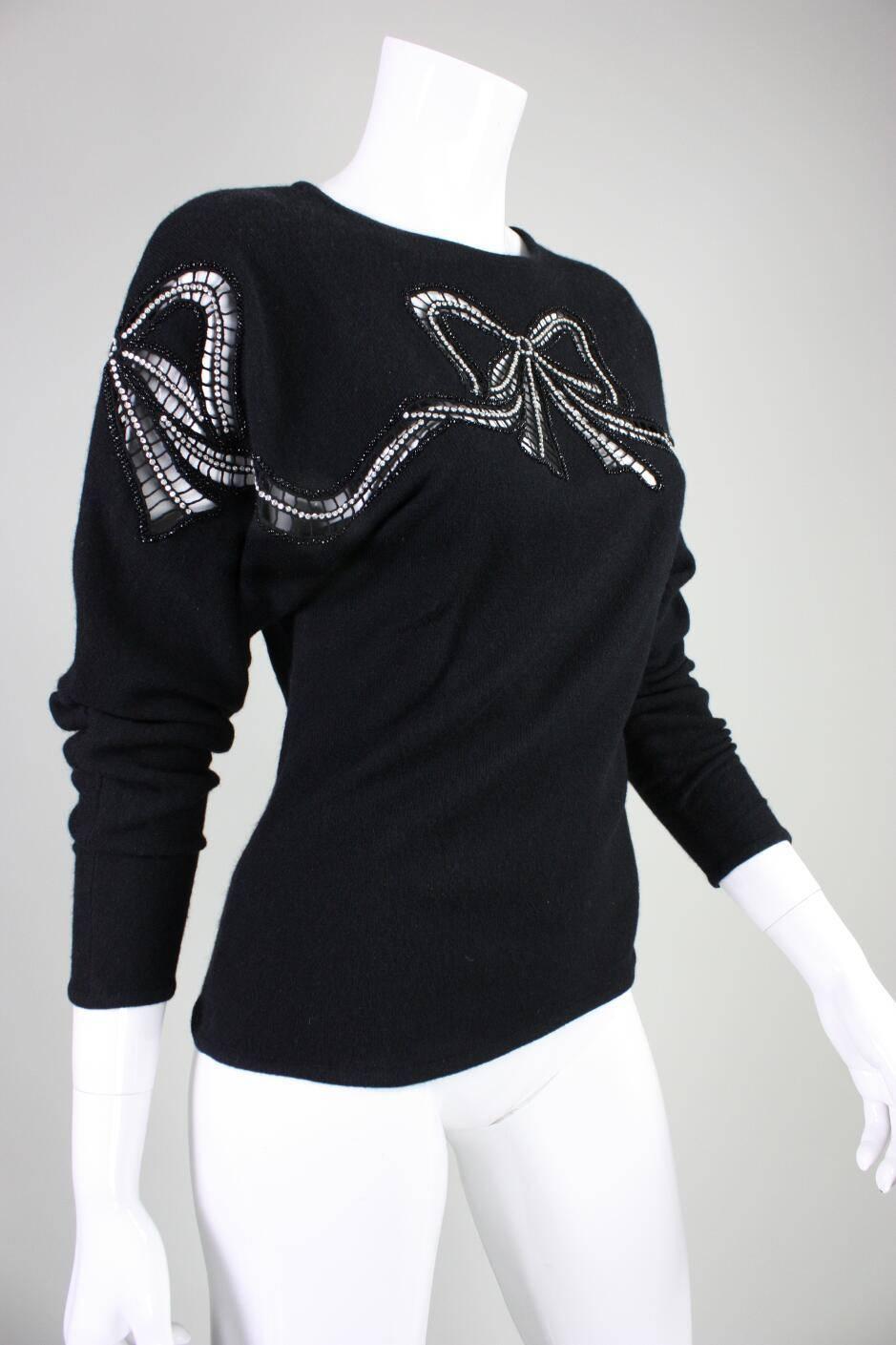 Vintage sweater dates to the 1980's and is an unlabeled Valentino that retailed at Amen Wardy. It is made of soft black wool with large openwork bows that extend from the front and around the shoulders to the back. Cutouts are accented with black