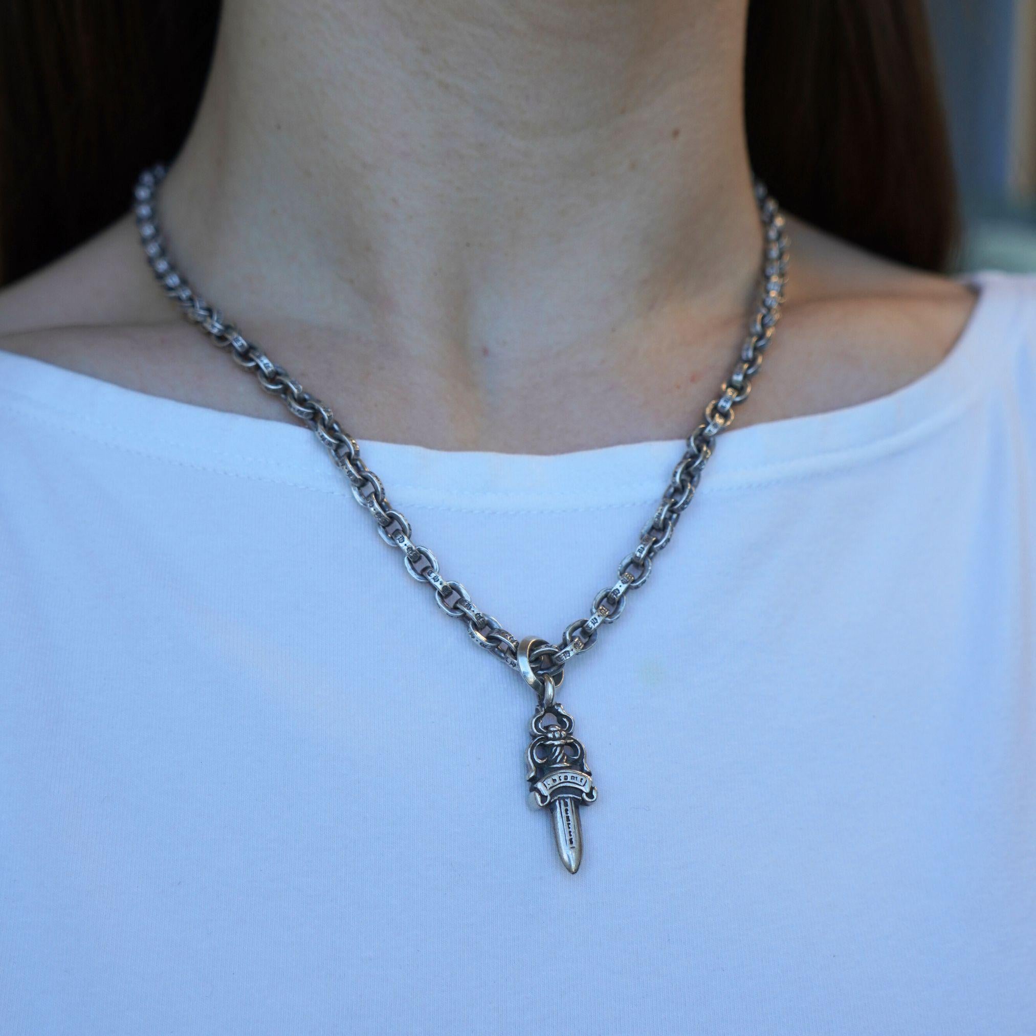 Questa collana con ciondolo in argento Chrome Hearts è dotata di una catena di 19 pollici e di un ciondolo a forma di pugnale che misura 1 pollice e mezzo di lunghezza per 1 pollice e mezzo di larghezza. Le maglie della catena sono decorate con
