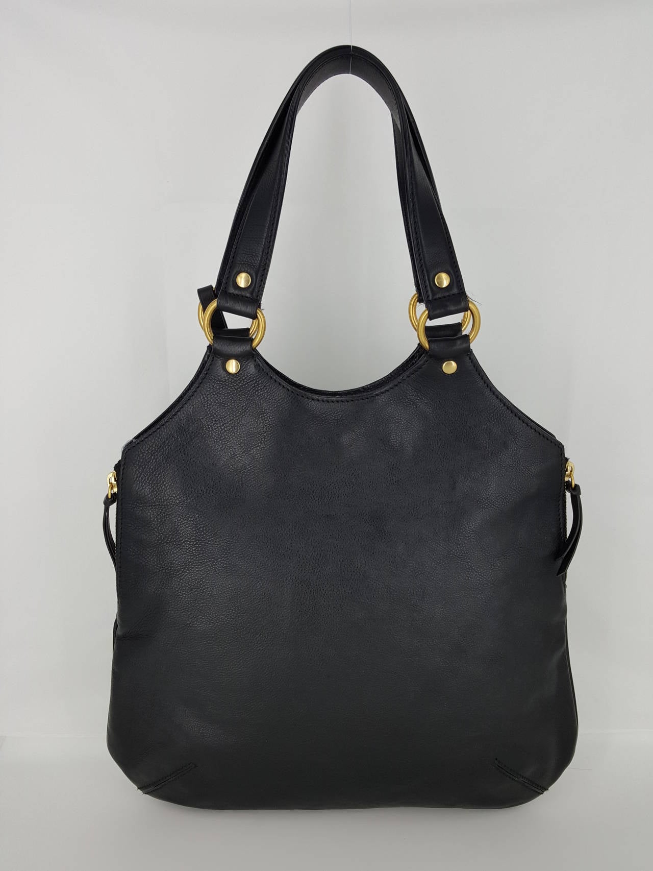 Offered for sale is this black leather YSL Yves Saint Laurent Tribute Bag.  This is done in beautiful black leather and has a YSL Hang tag  logo adornment, dual handles, button closure, and 2 side zippers.  The interior is black satin with 1