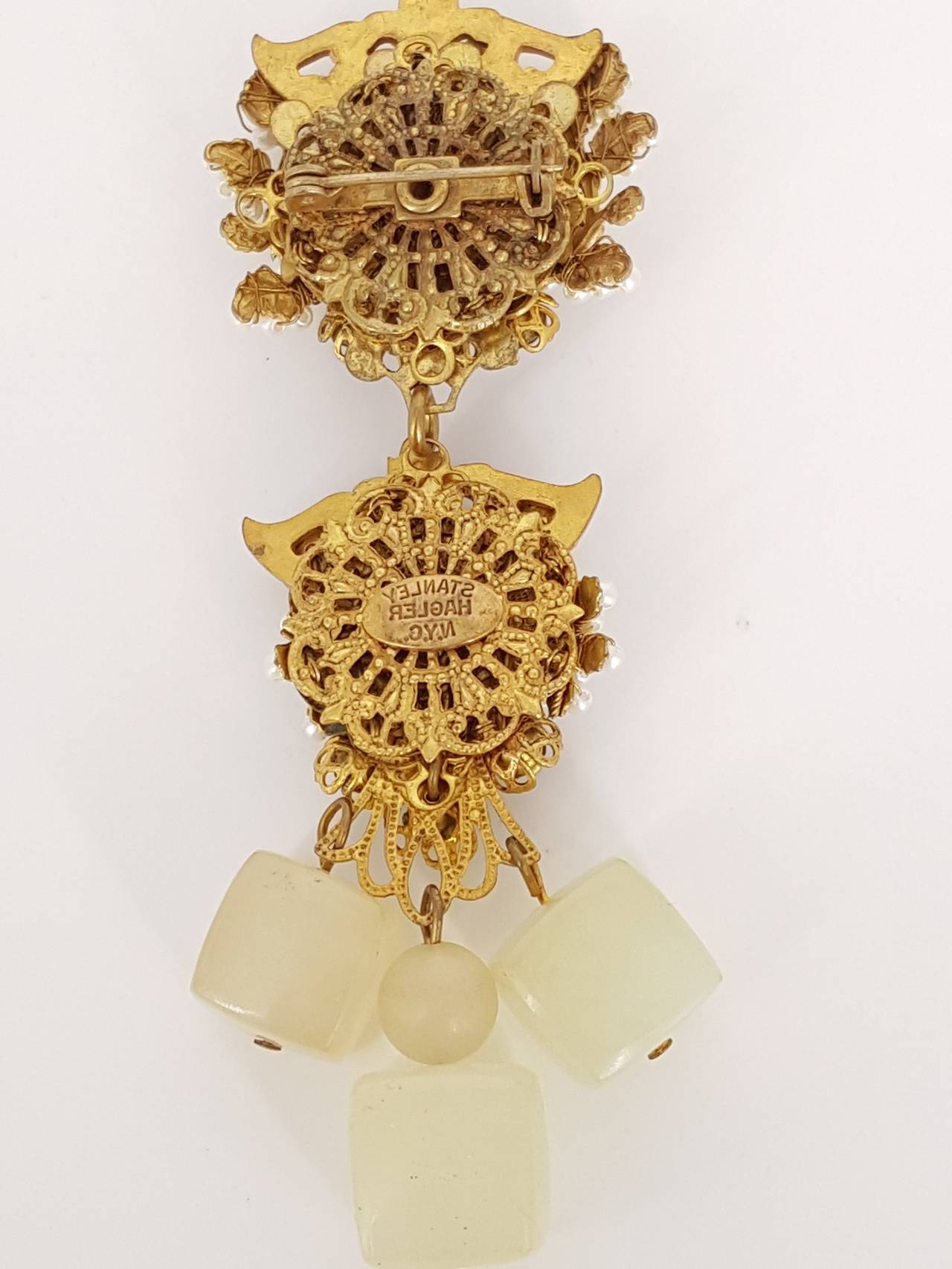 Offered for sale is this lovely Stanley Hagler of N.Y. hanging brooch.  The workmanship is gorgeous.  This is a 2 tier brooch with hanging Lucite squares that move.  The upper portion has a large soft green cabochon stone surrounded by filigree,