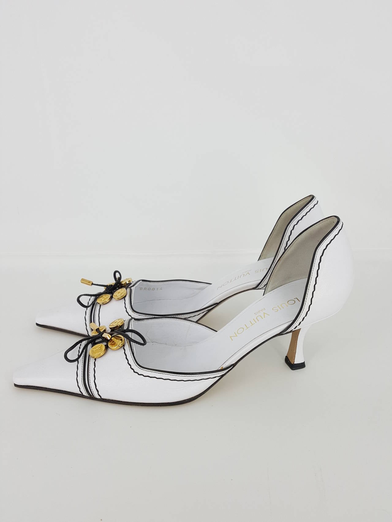 Offered for sale are these stunning Louis Vuitton white leather with black trim pumps in size 38 1/2.  The front has 4 gold logo charms and a thin black tie with gold ends.  They are cut out on the sides and have a 2 1/2