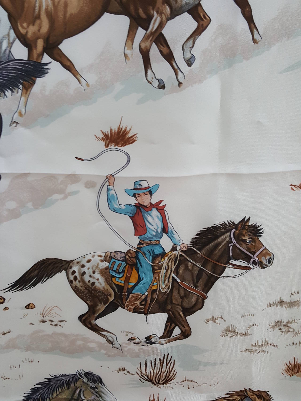 Offered for sale is this lovely Hermes scarf by Robert Dallet from 1993/1994 in
white, rich brown tones, gray, and with the colored cowboys in in blue and rust.
The mustangs are depicted beautifully and the added colors really make the scarf come