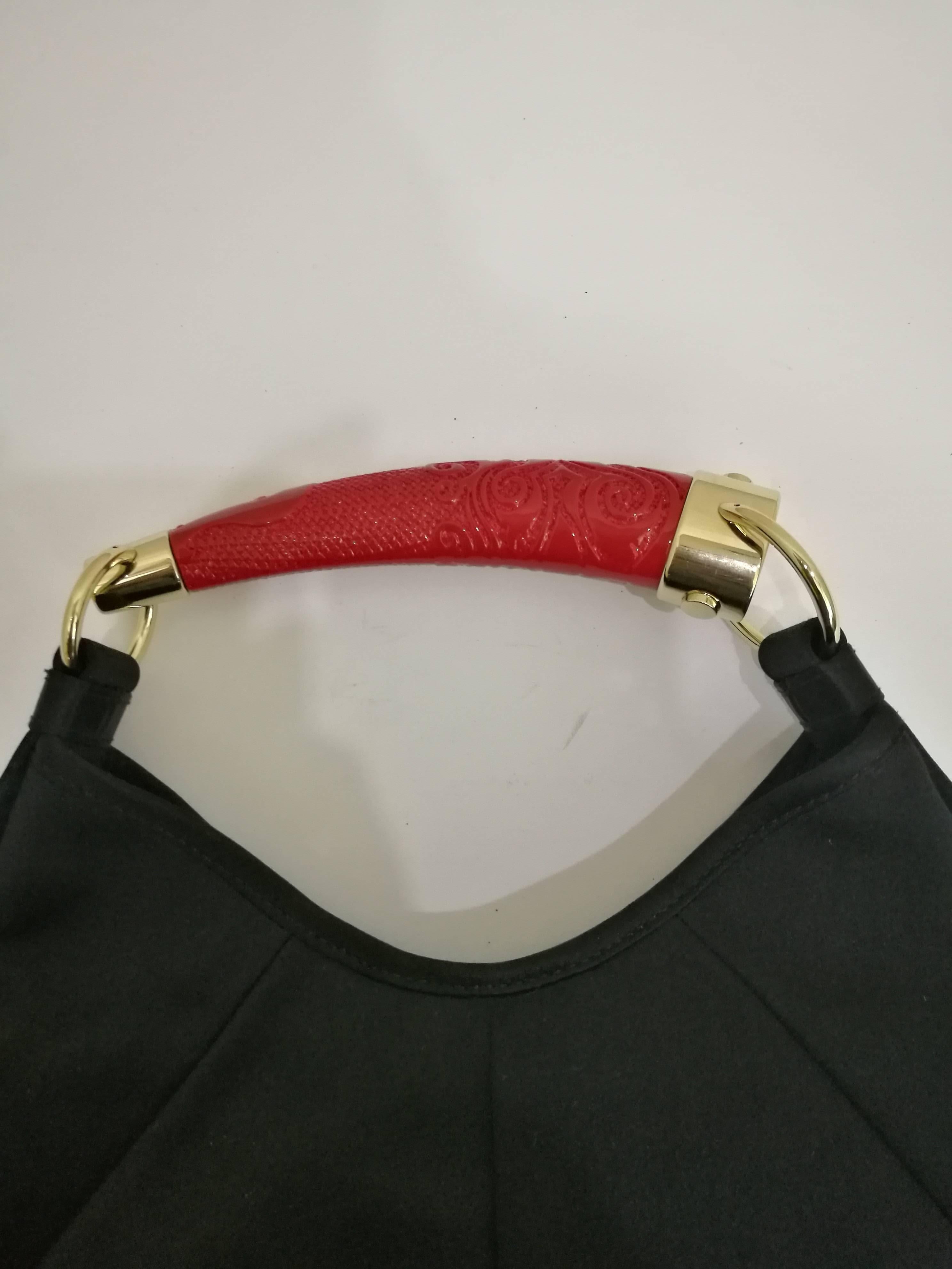Shoulder bag Yves Saint Laurent Rive Gauche Mombasa model in black leather embellished with a gilded metal handle and red resin horn so chiseled arabesque motifs in relief.
- The bag is centered round a small medallion in red resin holding a black