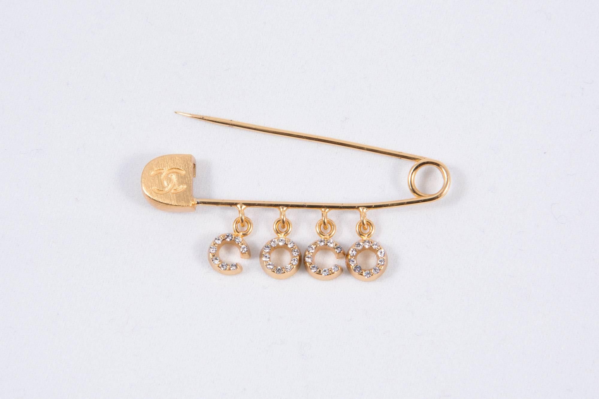  2001s Chanel Coco crystal strass & gold tone brooch featuring a safety pin shape, Chanel signature engraved on the reverse of the pin. 
A beautifully and practical brooch for securing a scarf, sweater or on a suit.
Length:1,9 in. (5cm) X 0,8in.