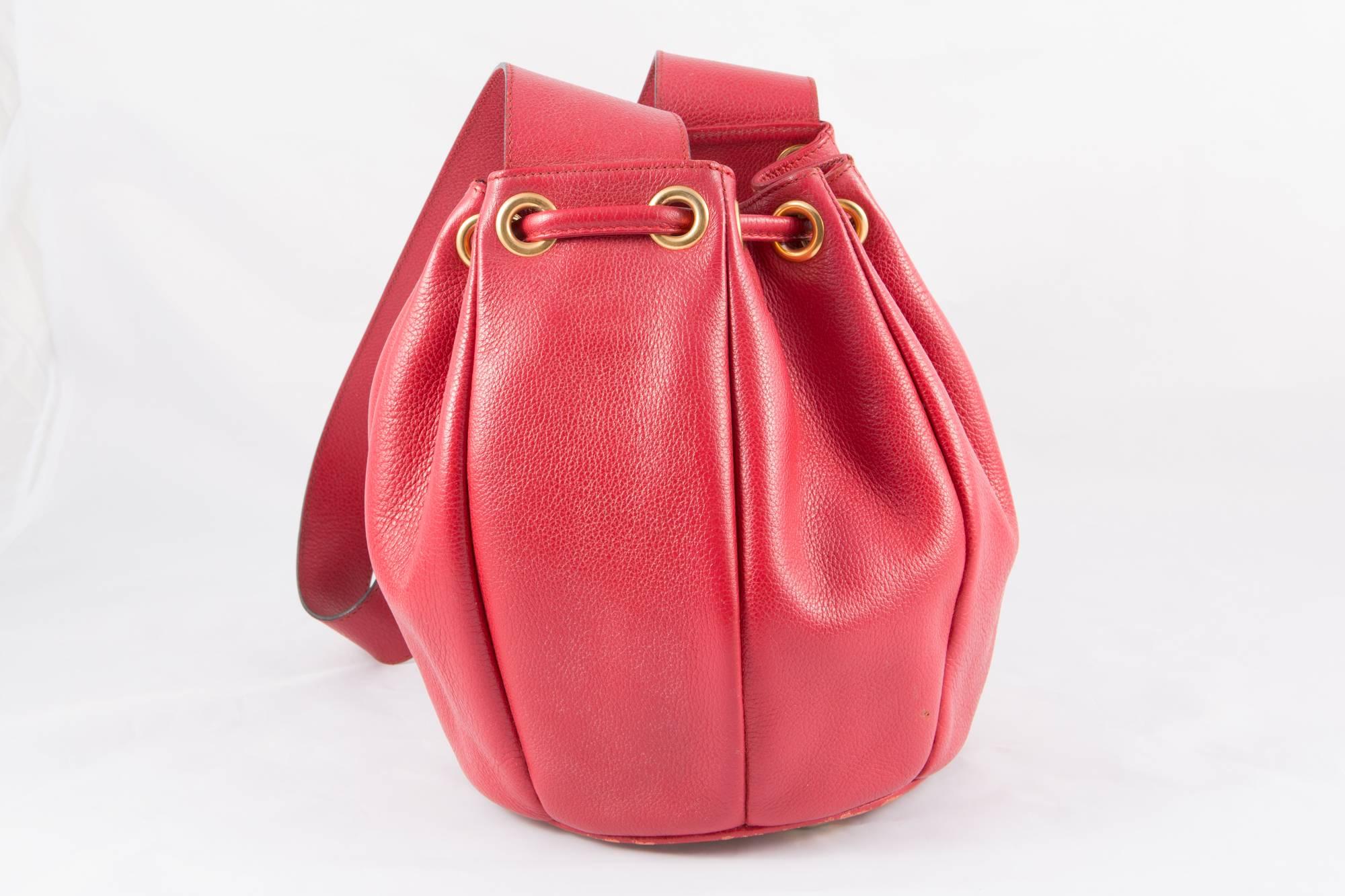 1990s red Saint Laurent bucket leather shoulder bag featuring a bucket style, a pebbled leather texture, a shoulder strap, a drawstring fastening, a main internal compartment, gold tone hardware and an outside front embroidered YSL. 
In excellent