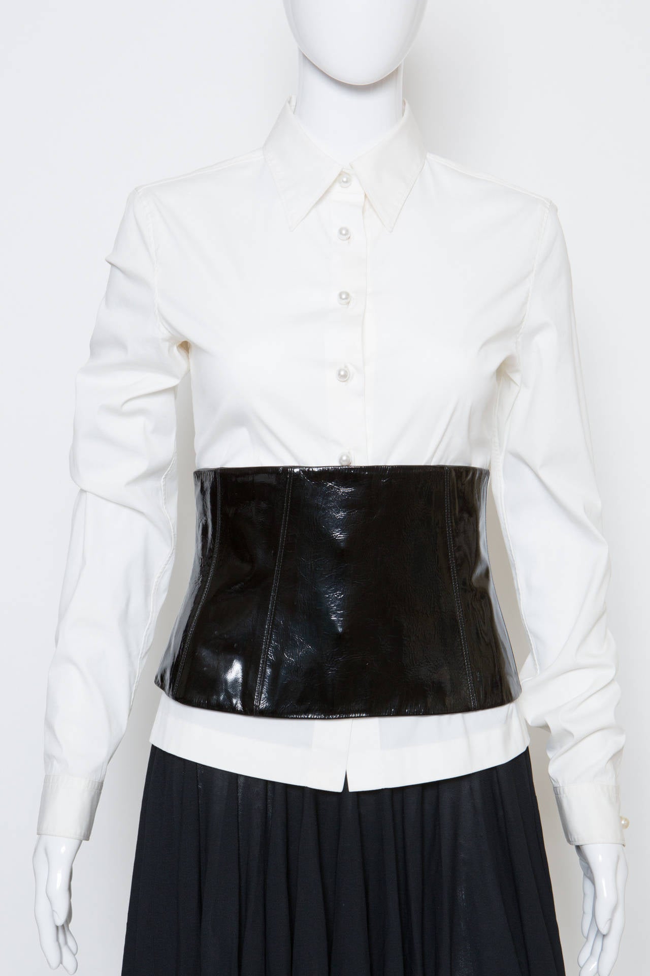 White cotton shirt from Chanel with pearl-tone buttons at front opening and cuff links with silver-tone and pearl-tone beads. This very chic shirt comes with a black vinyl leather corset belt (21cm width) with a silk lining and a center back zip