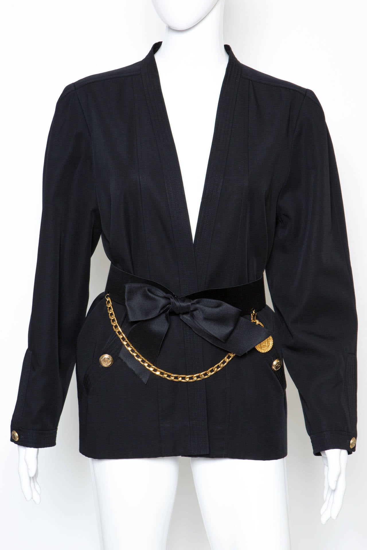 Gorgeous black wool kimono-style jacket from Chanel featuring an open front, front button pockets, fully lined, long sleeves and button cuffs. The jacket comes with a  black Chanel front satin silk bow detail, a logo charm and a detachable gold-tone