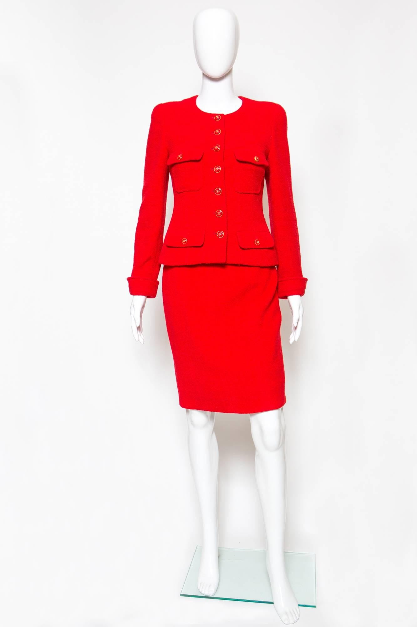 1990s Chanel iconic red wool boucle skirt suit.  
The jacket has a fitted round neck with center front gold-tone logo buttons opening, four patched pockets,  a silk logo lining, and a 24kt gilded gold hardware chain in the bottom lining. The jacket