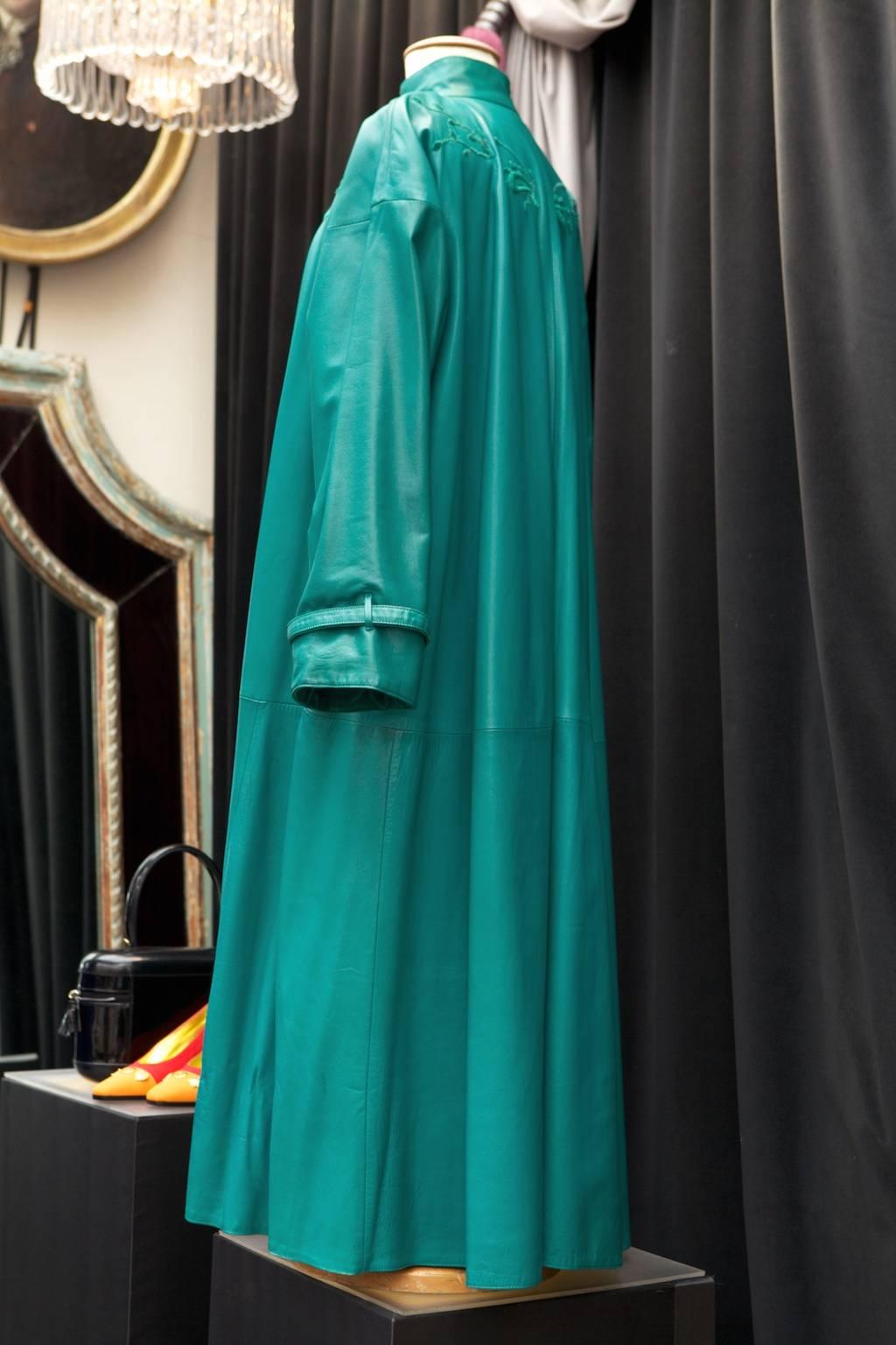 GIANNI VERSACE Long green calf leather coat embroidered on the chest and at the rear with green thread figuring 'cashmere' and vegetal motif. The coat fastens with three buttons covered with braided straps of green plastic. 
The coat is fully lined