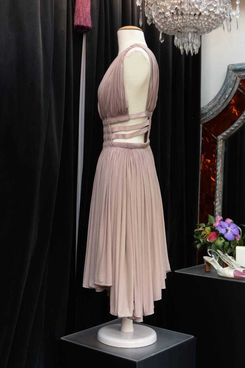 ALAIA PARIS (Made in Italy) Mini dress in a antique greek style composed of light pink cupro. 

The dress is belted at the waist by several elastic straps. 
The skirt part is comprising of voluminous pleated cupro cut asymmetrically. 

Ecru lining