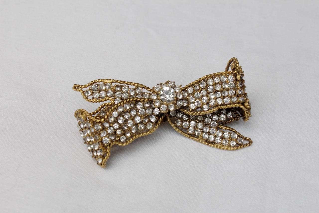 CHANEL Rare brooch Chanel from the 1960s-1970s in a shape of a bow made of gilt and paved with white rhinestones. Probably a work by Gripoix for Chanel. 

Signed on plaque at the rear. 

The fastener is a bit difficult to open.