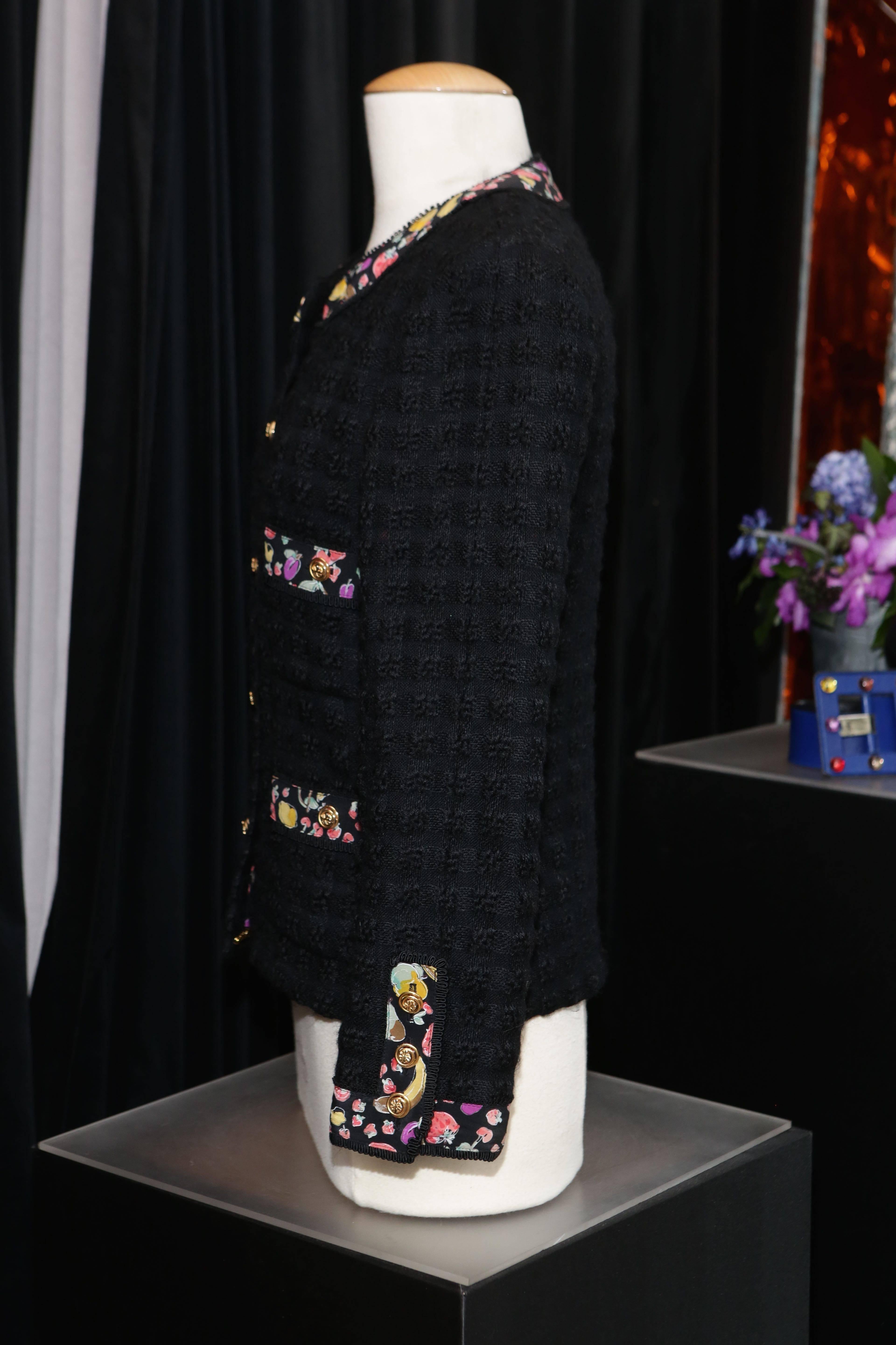 CHANEL BOUTIQUE Black tweed jacket adorned with a black silk galloons printed with colorful fruit pattern 

The galloons are displayed around the round neck, the lining, the cuffs and the four pockets. 
The jacket features also gold-tone metal