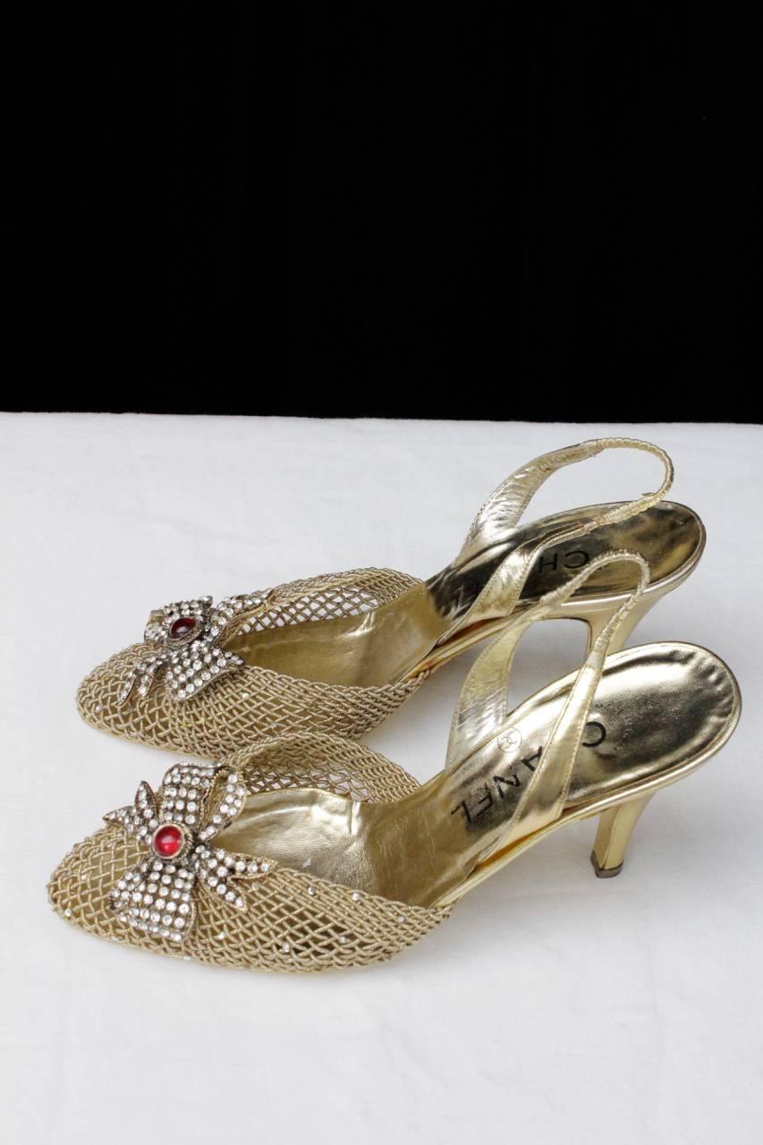 CHANEL (Made in Italy) Absolutely astonishing slingback shoes in gold tone leather, threads covered with lamé braided and adorned with a bow in metal, crystals and a red glass paste cabochon. 

The gold threads are also adorned with several