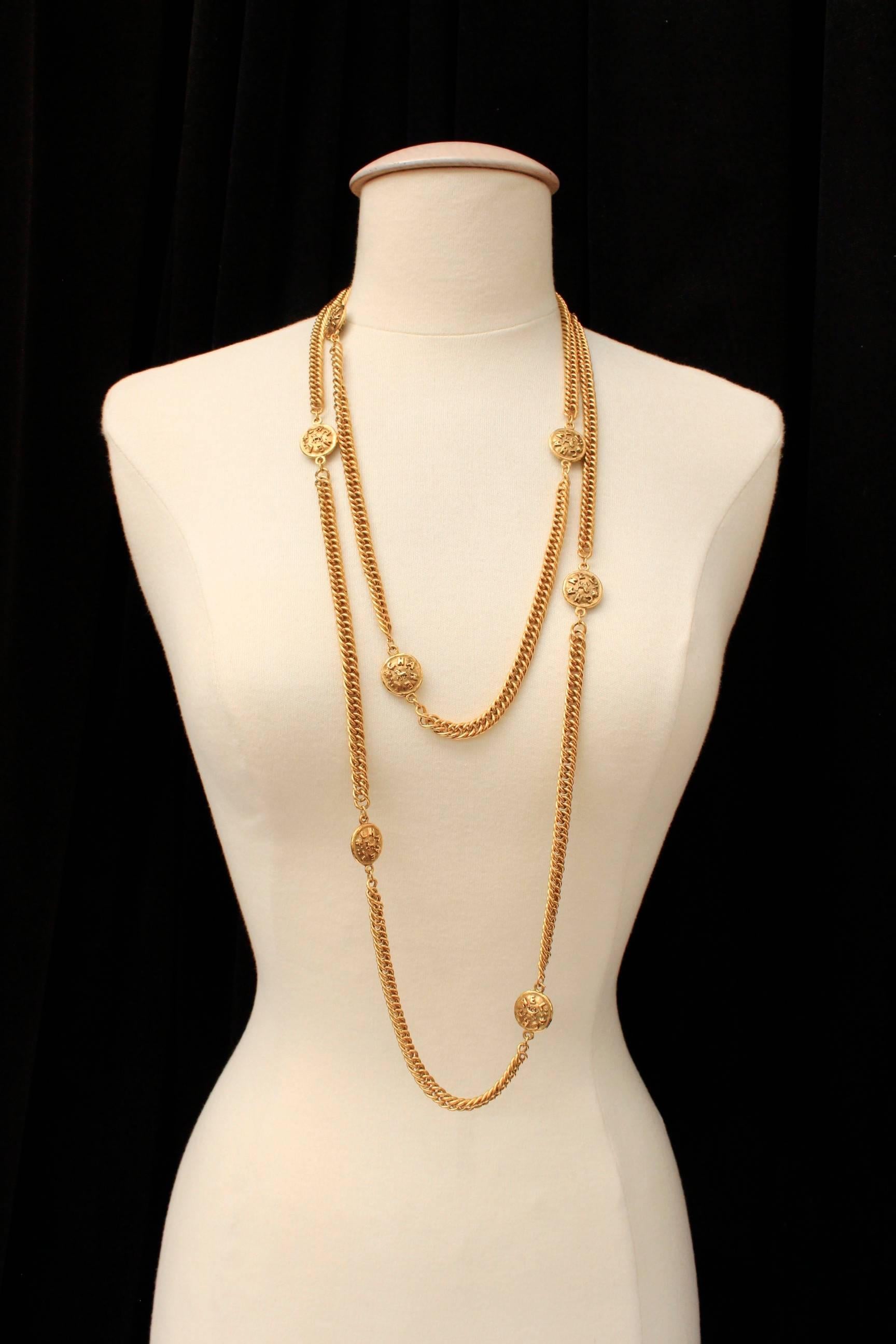 CHANEL (Made in France) Gilt metal long necklace composed of gilt chain alternated with round medals struck with the brand name and a lion silhouette. 

The necklace is signed on plate, collection 2 cc 3 dating from the early 1990s.

Very good