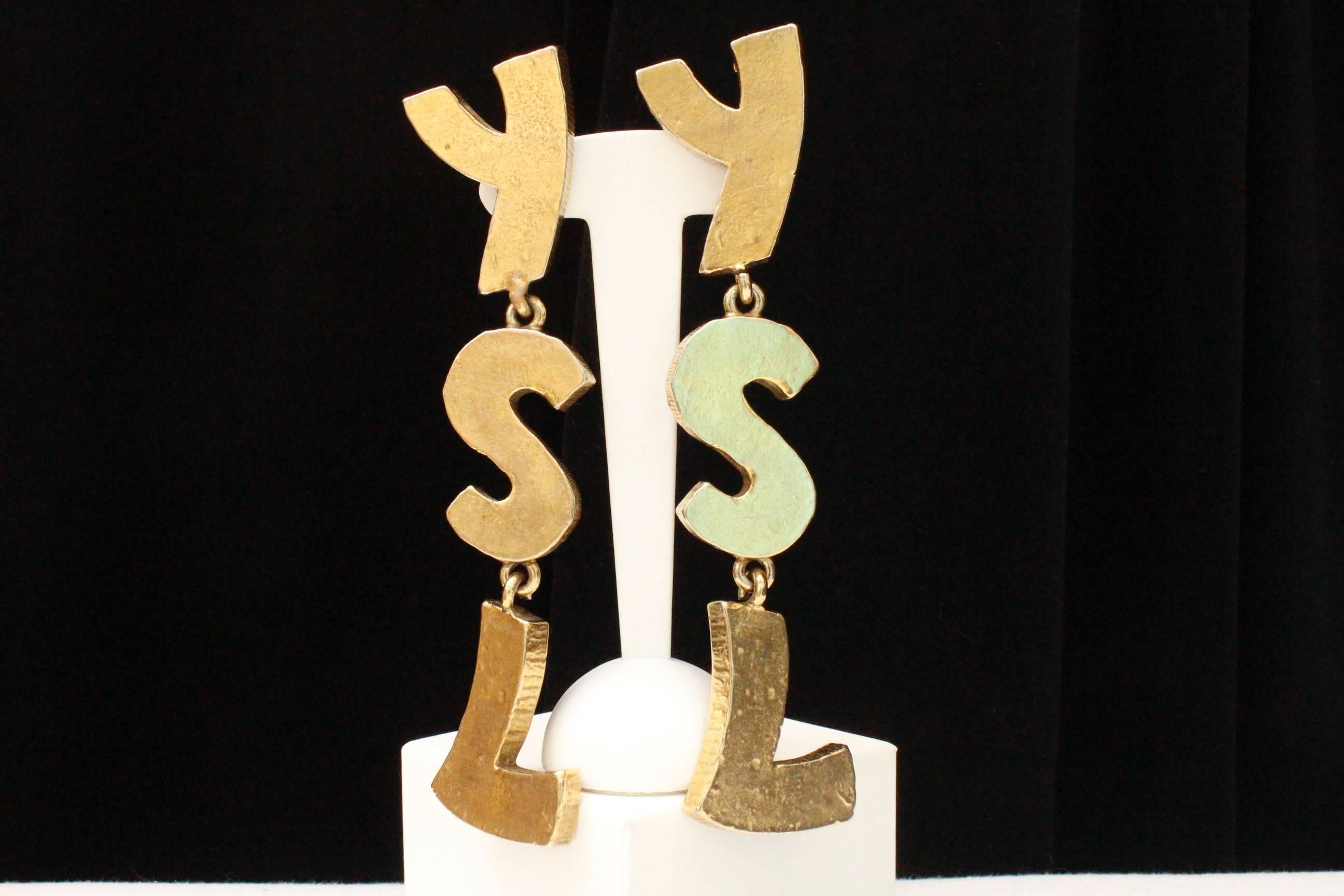 YVES SAINT LAURENT (Made in France) – Magnificent drop clip-on earrings composed of  the three oversized initials YSL linked together, made of hammered hollow gilded metal.  Signed at back.

Iconic and spectacular piece from the 1990s.

Length 14 cm