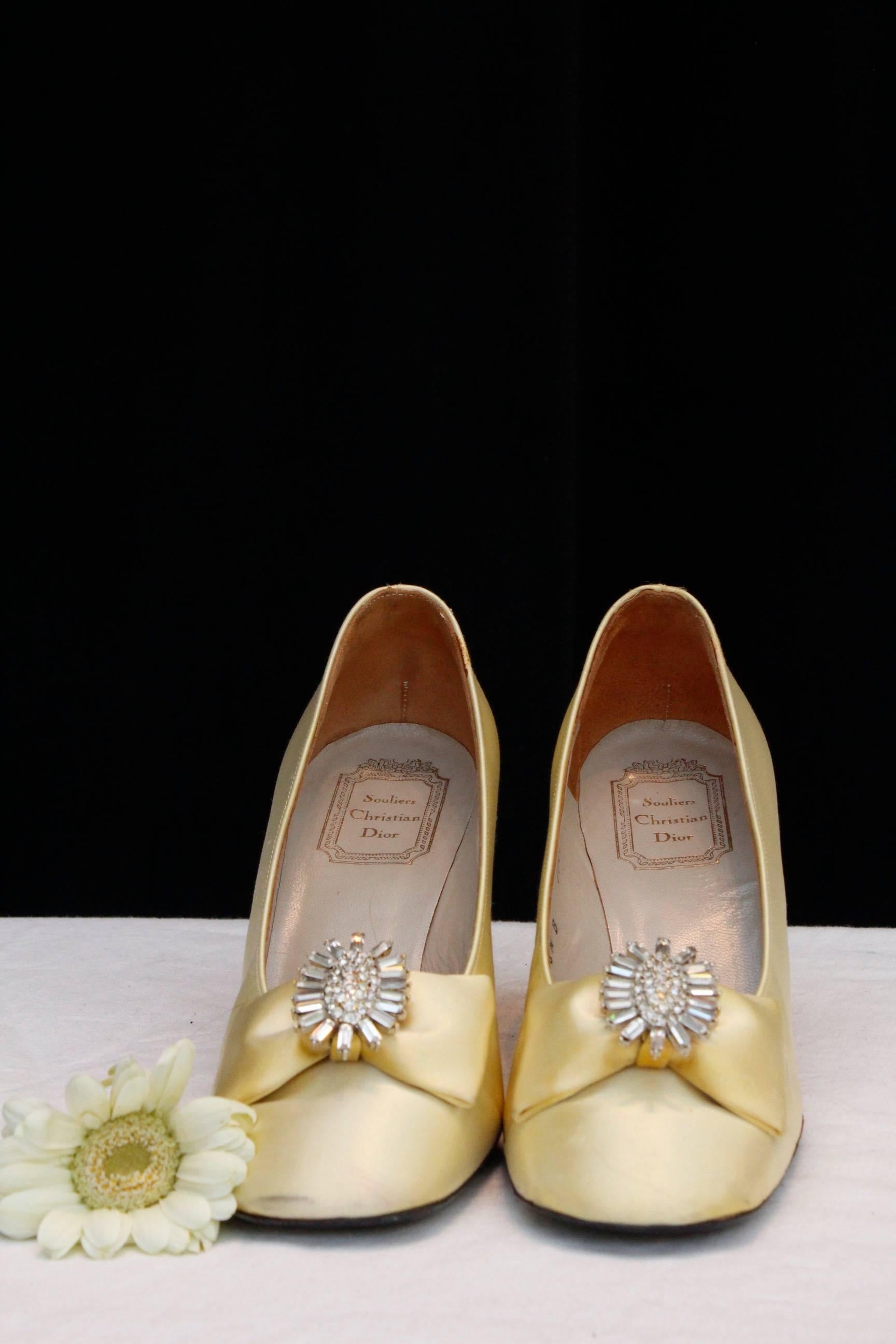 CHRISTIAN DIOR SOULIERS – Amazing square heels pumps in light yellow satin embellished with a satin bow and a stylized gilded metal bow paved with marquise cut rhinestones. Beige leather lining, black leather outer sole. Size 5.5, 37 FR.

Heels 8 cm