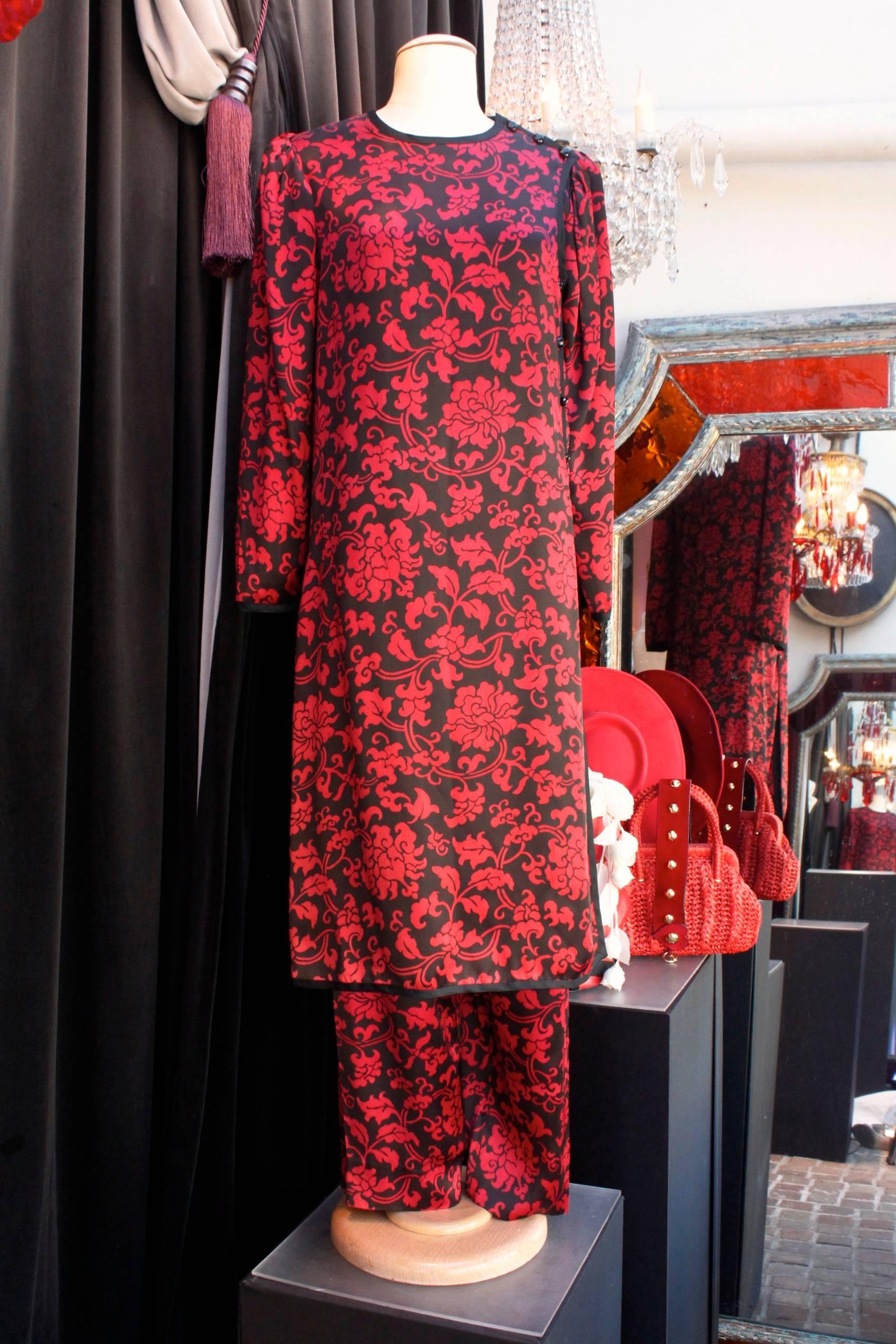 YVES SAINT LAURENT (Made in France) Set comprised of a tunic and slacks in red and black  silk with arabesque floral pattern. Long sleeves tunic inspired by traditional Chinese tunics, trimmed with black  braid, and closing with a long series of