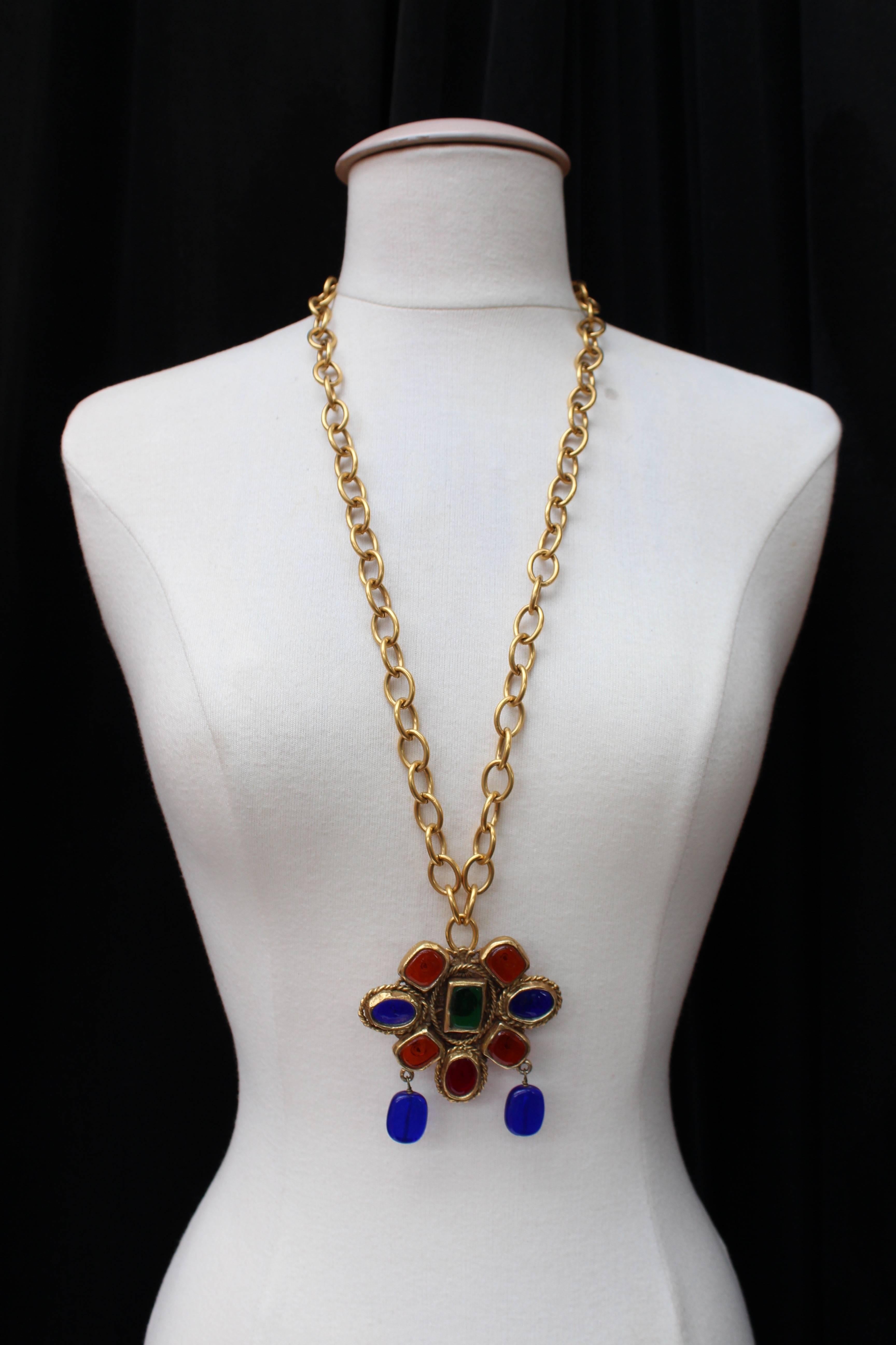 CHANEL (Made in France) Long necklace composed of a gilded metal chain and a pendant paved with glass paste cabochons in sapphire, ruby, honey and emerald colors. Ring clasp.

1984 piece signed at back of the medallion.

Very good