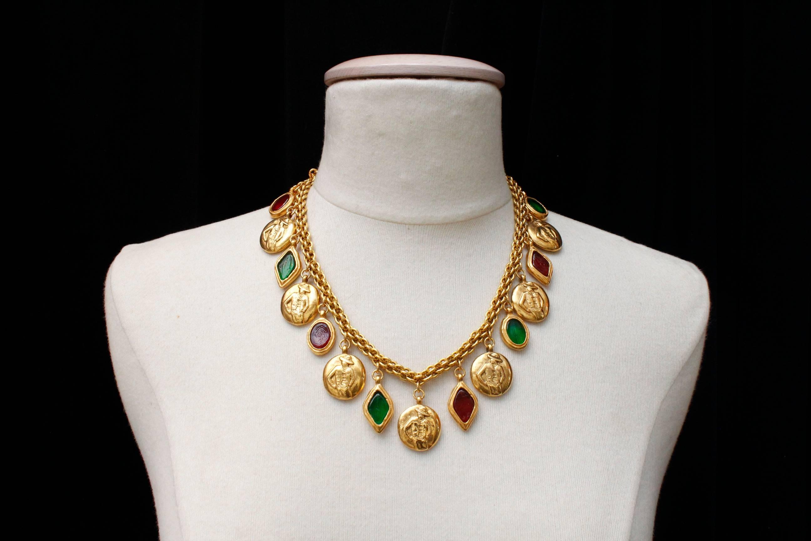 CHANEL (Made in France) Short necklace composed of  a textured gilded metal chain from which hang a series of triangular pendants paved with emerald cabochons, oval pendants paved with ruby cabochons and round medals showing the effigy of Gabrielle