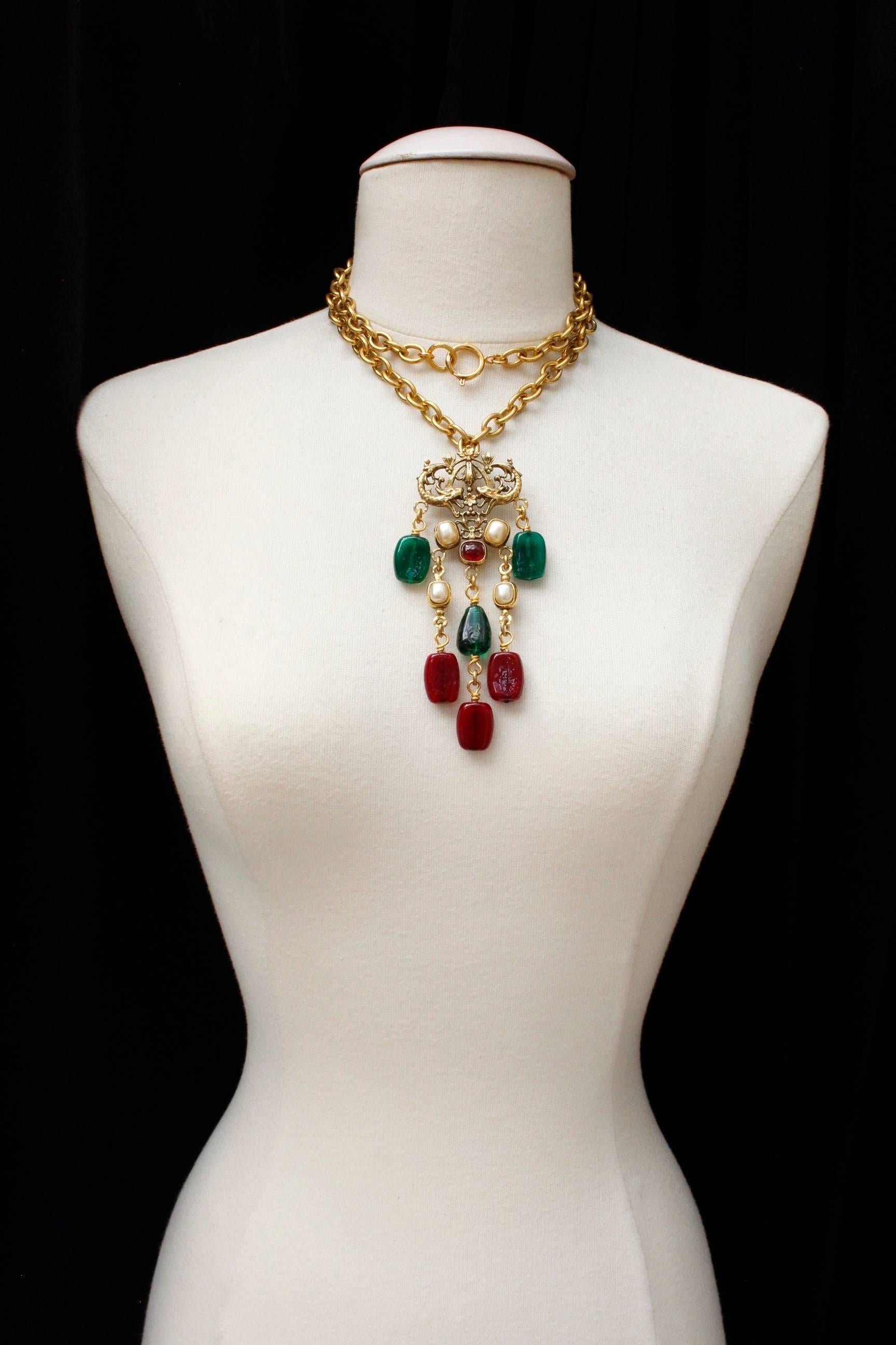 CHANEL (Made in France) Long necklace consisting of a gilded metal chain and a baroque pendant. The pendant is made of faux pearl cabochons, red and green glass paste cabochons and a basis in chiseled gilted metal. 

Signed at back of the