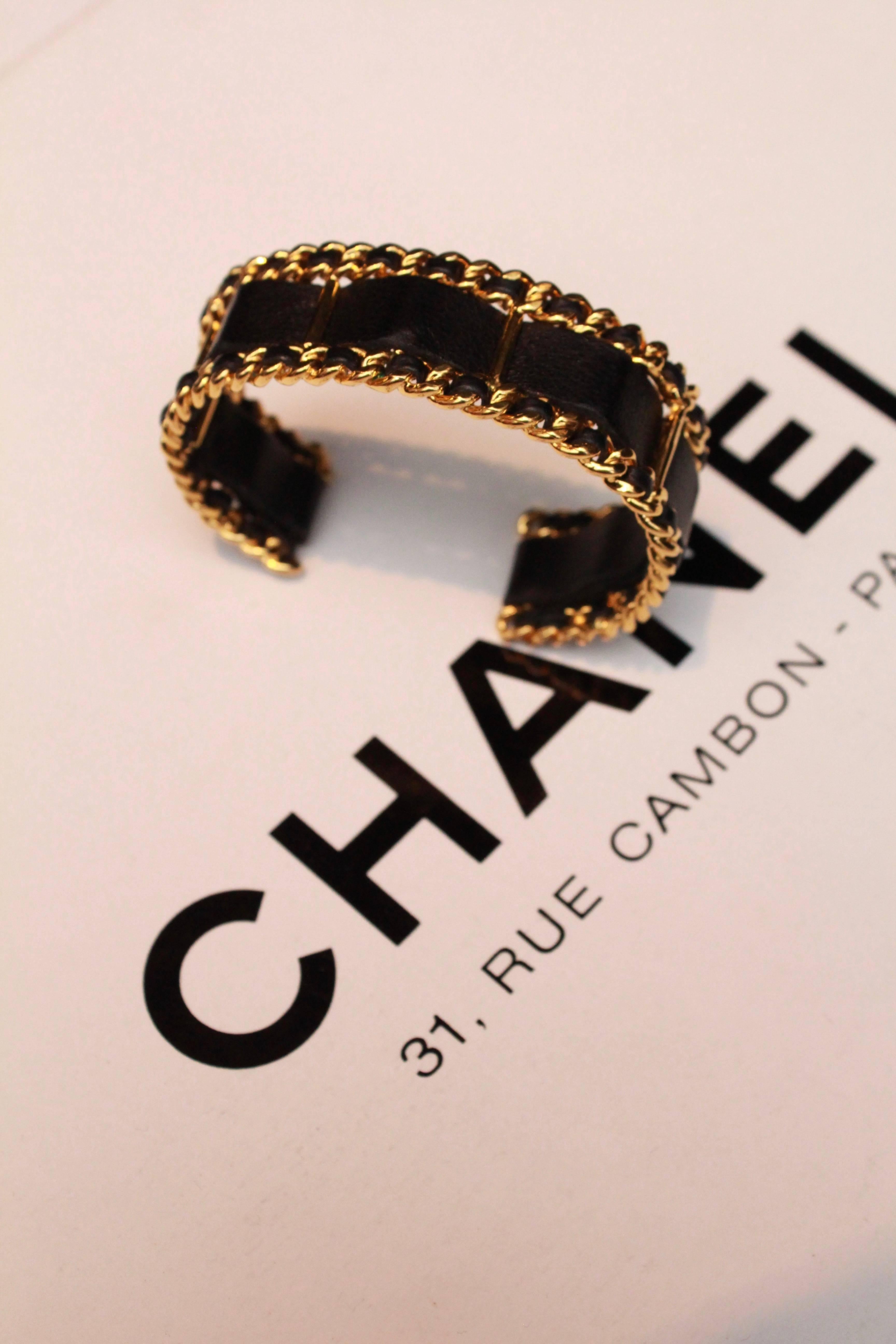 CHANEL (Made in France) Cuff bracelet, comprised of gilded metal base with black leather interwoven throughout. The edges of the bracelet are comprised of gilded metal chain with an interwoven leather cord, the center features a black leather