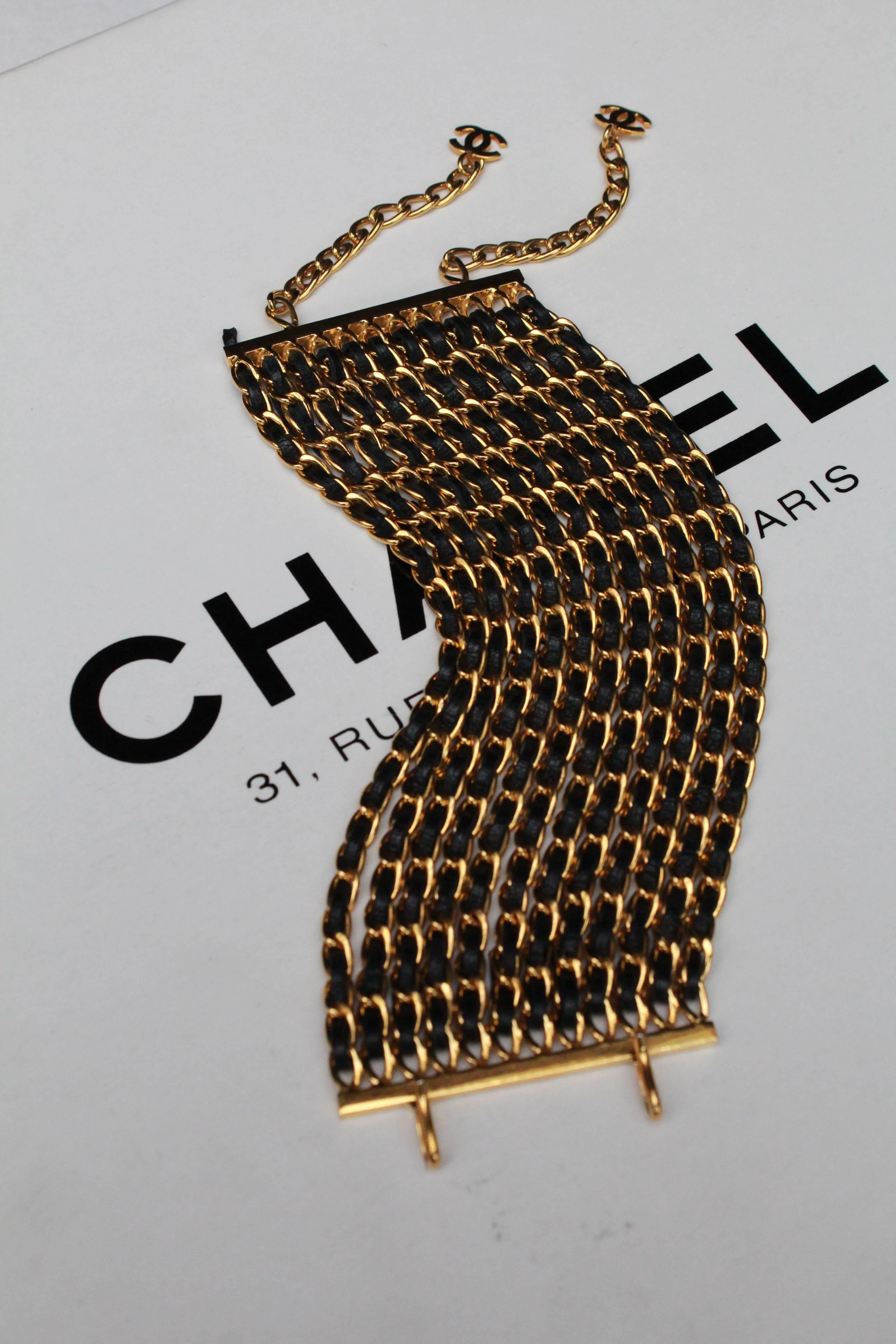 CHANEL (Made in France) Wide cuff bracelet comprised of twelve gilded metal chains. Each chain is interwoven with a black leather cord, using the same techniques and materials as the iconic Chanel handbag. The bracelet can be adjusted by two gilded